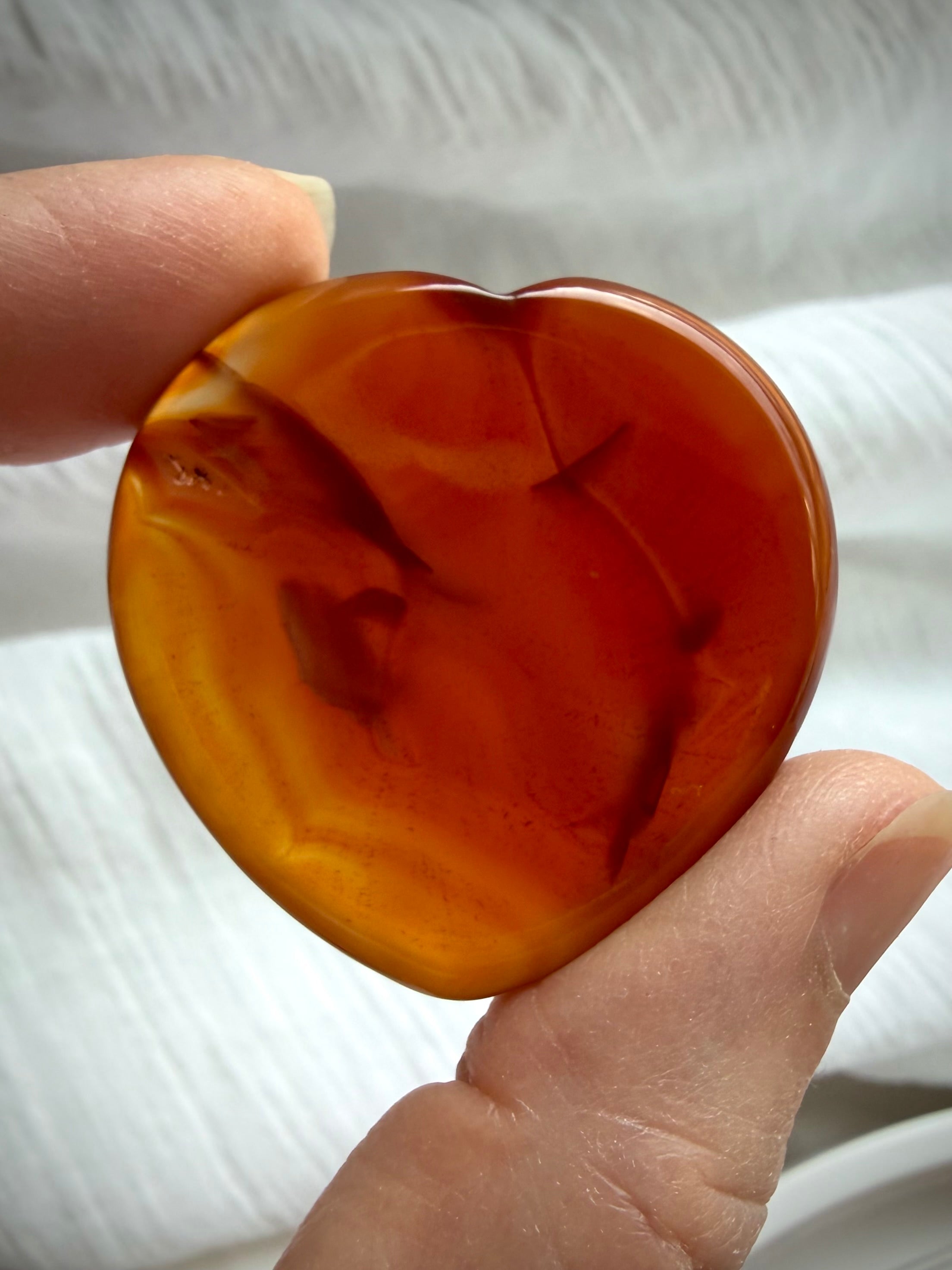 Translucent Carnelian heart worry stone with amber-orange color, darker natural inclusions and glossy polish
