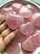 Palm-sized Rose Quartz heart held in hand showing natural pink color, translucence and polished finish