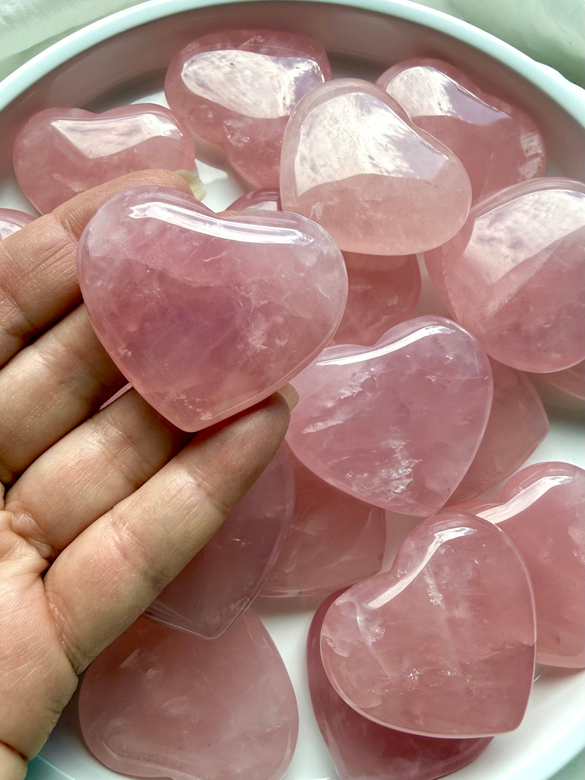Palm-sized Rose Quartz heart held in hand showing natural pink color, translucence and polished finish