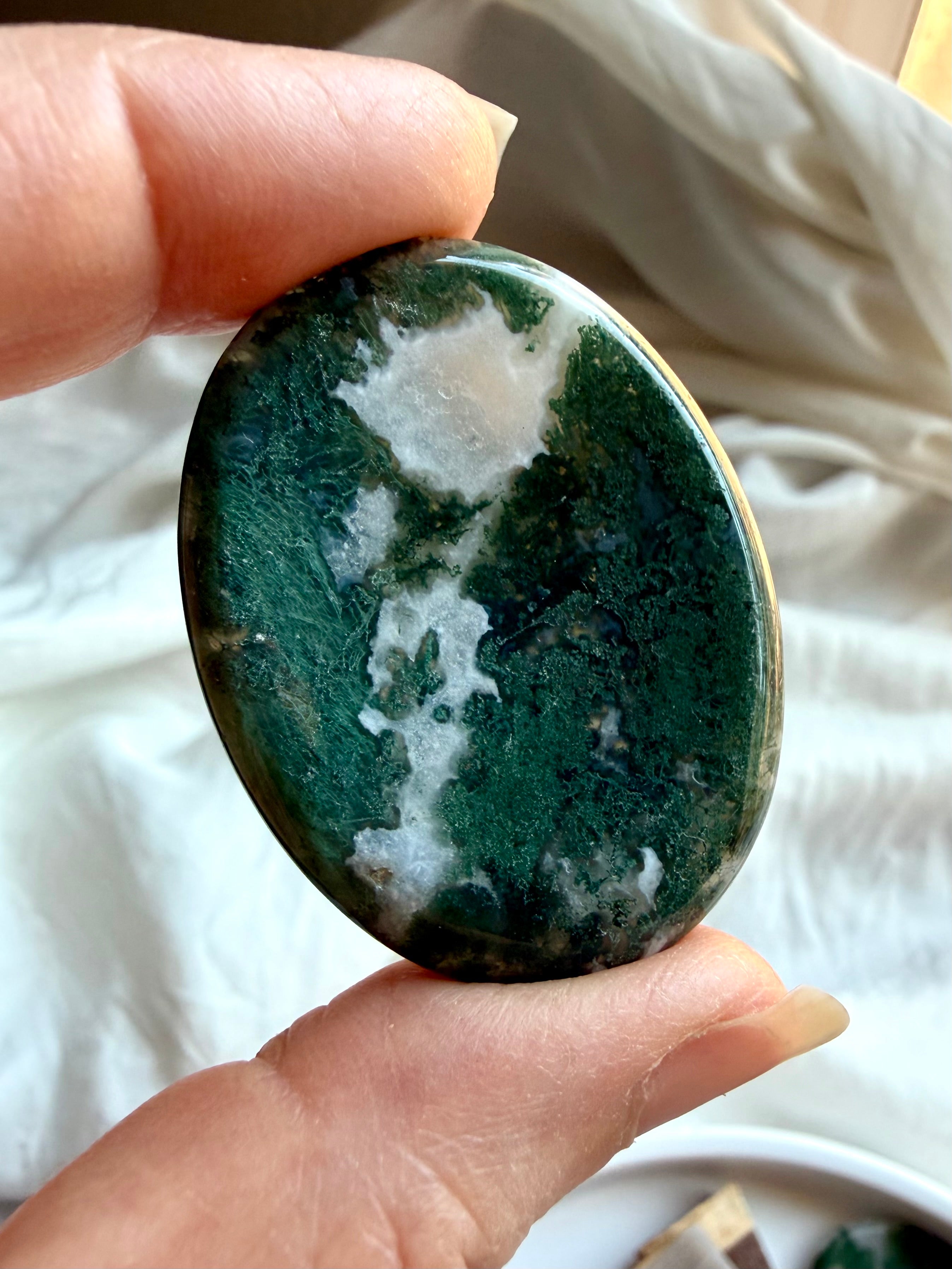 Moss Agate oval worry stone held in hand with translucent quartz, forest green inclusions and landscape patterns