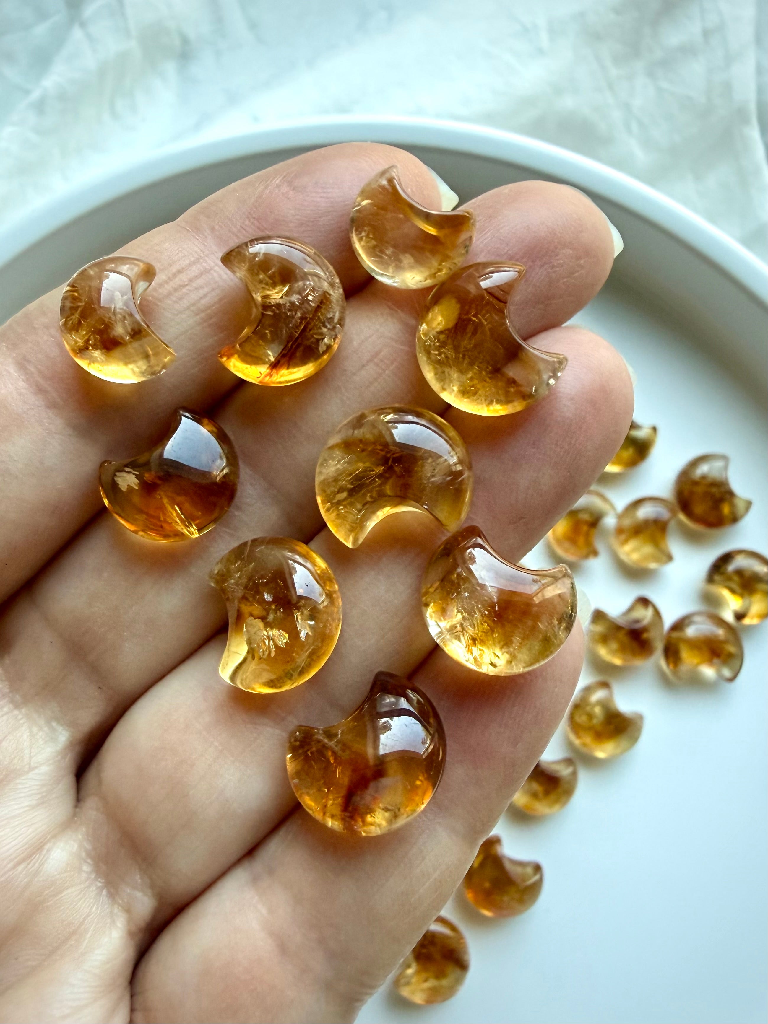 Mini Citrine moon carvings held in hand showing their tiny size, warm amber color and glossy polish