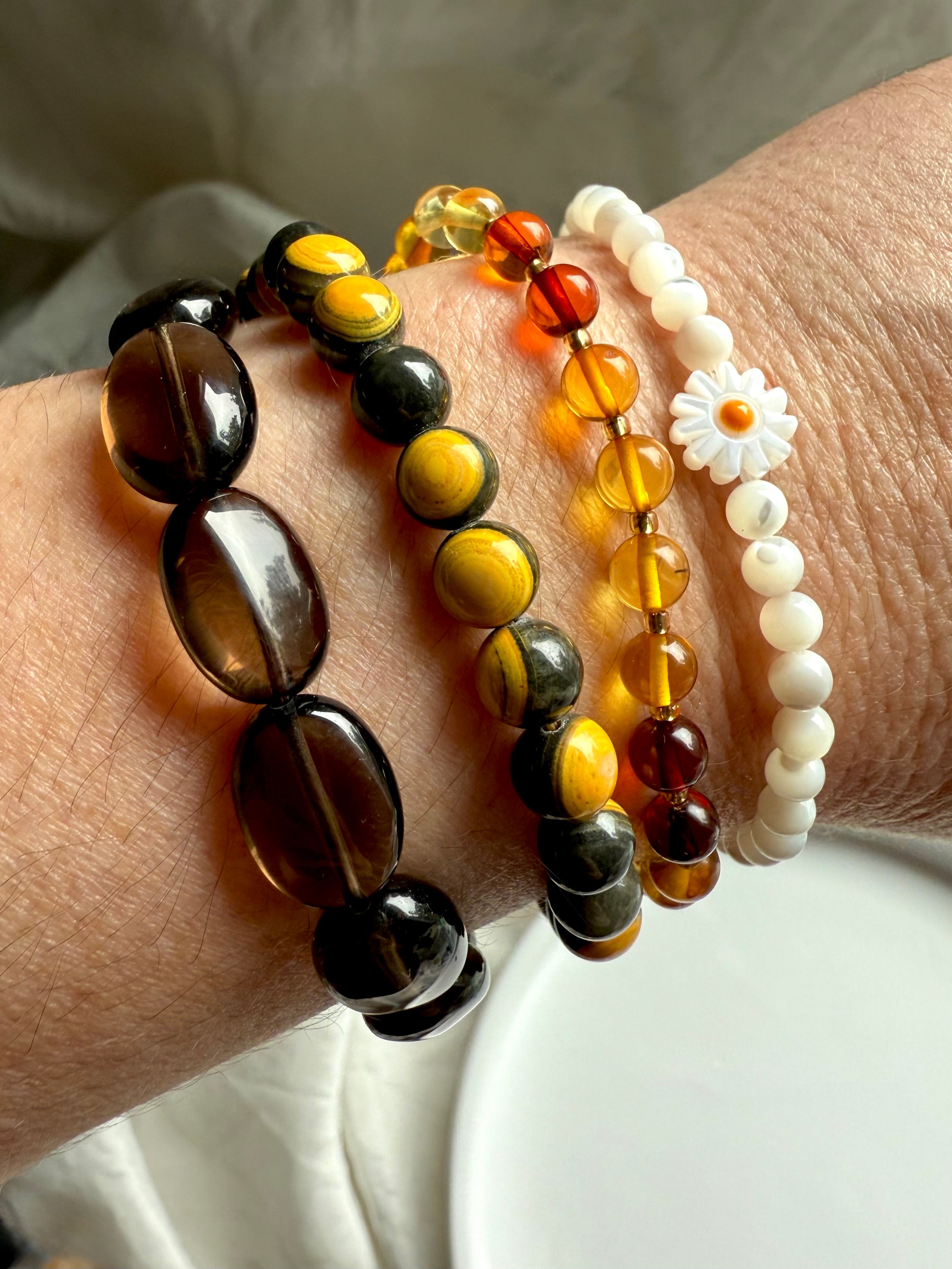 bumblebee jasper bracelet stacked with smoky quartz and mother of pearl daisy bracelets, crystal arm candy for solar plexus healing, grounding, and joy