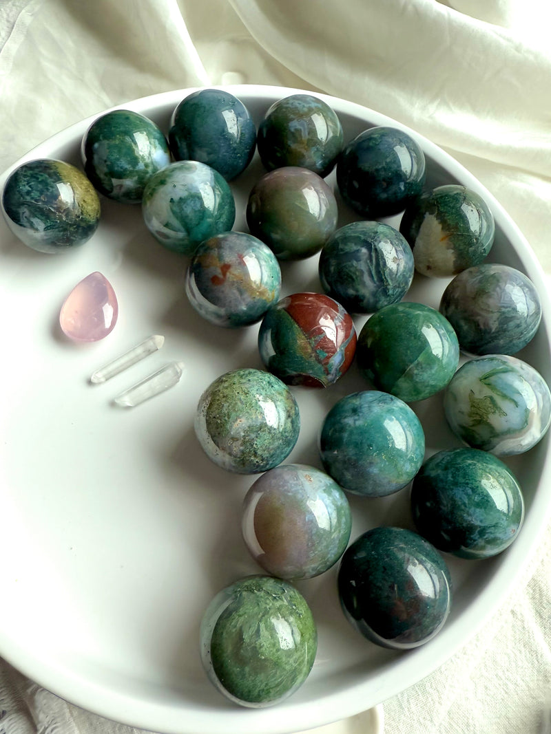 Colorful moss agate mini spheres shown on a white plate with some other crystals