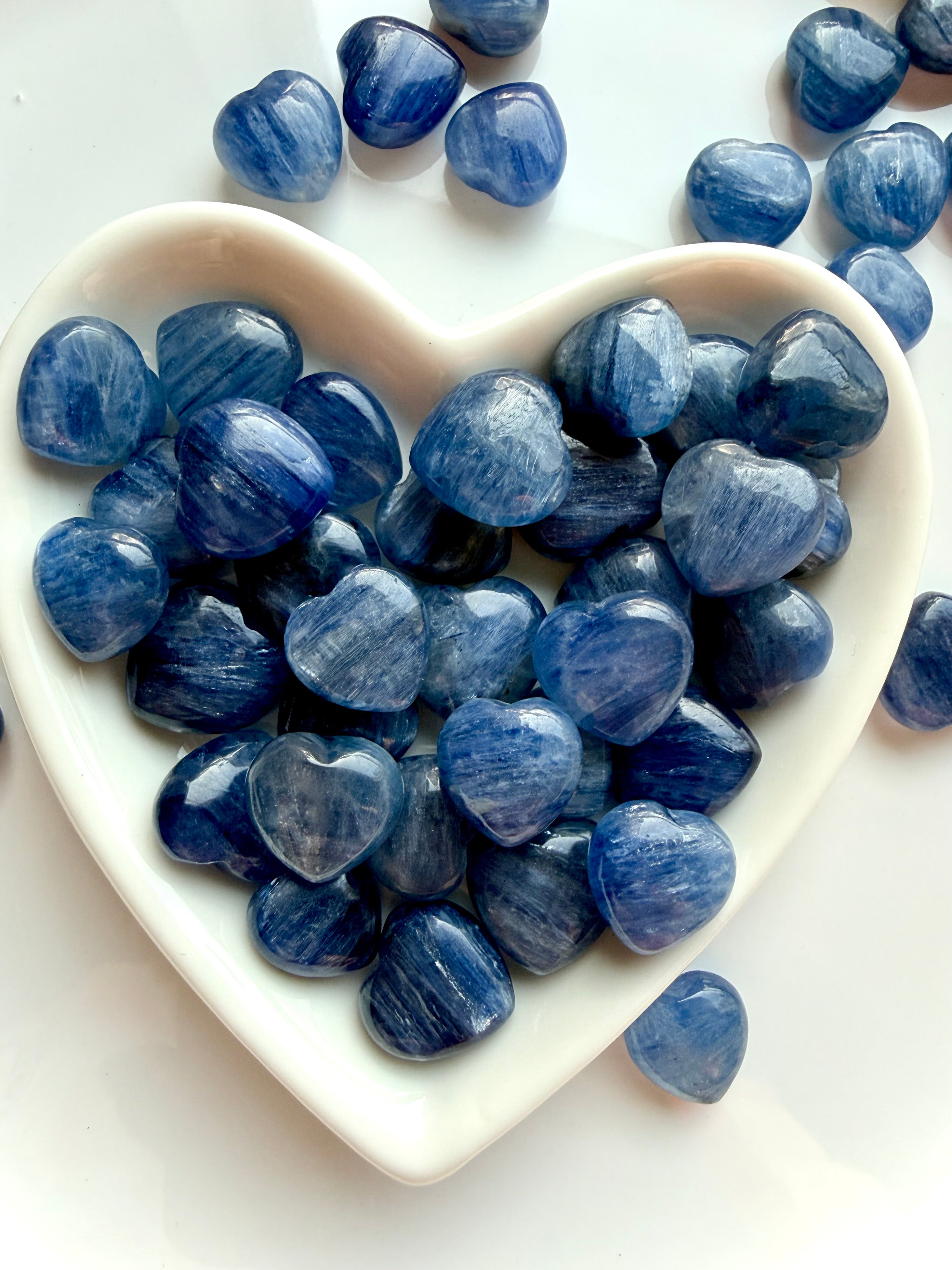 White heart bowl overflowing with mini Blue Kyanite crystal hearts, silvery blue shimmer stones for meditation and chakra healing