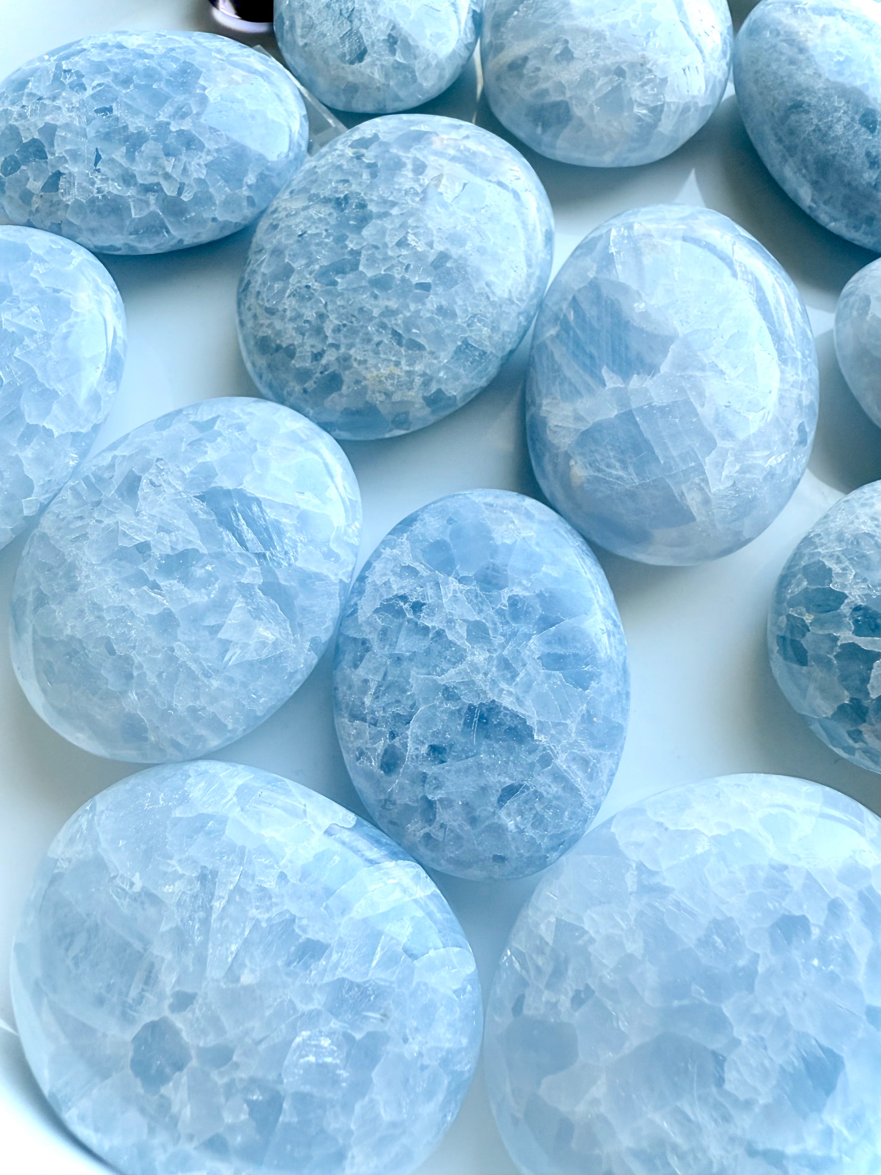 Arrangement of high quality Blue Calcite palm stones on a white plate — soothing crystals for peaceful communication and emotional balance 