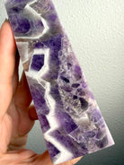 Chevron Amethyst crystal tower held in hand, revealing deep violet formations, intricate white quartz chevrons and natural crystal banding