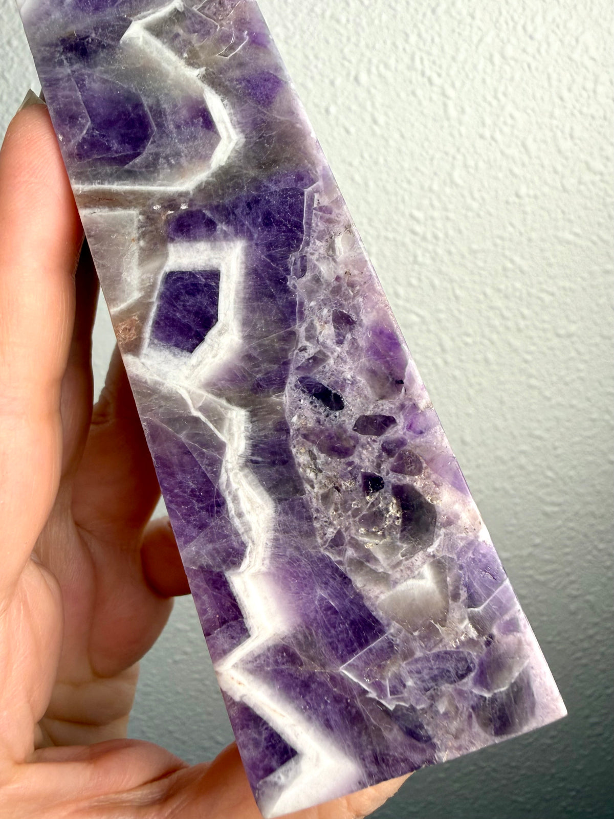 Chevron Amethyst crystal tower held in hand, revealing deep violet formations, intricate white quartz chevrons and natural crystal banding