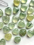 Variety of Prehnite gemstone hearts with green translucence and Epidote inclusions displayed on white plate.