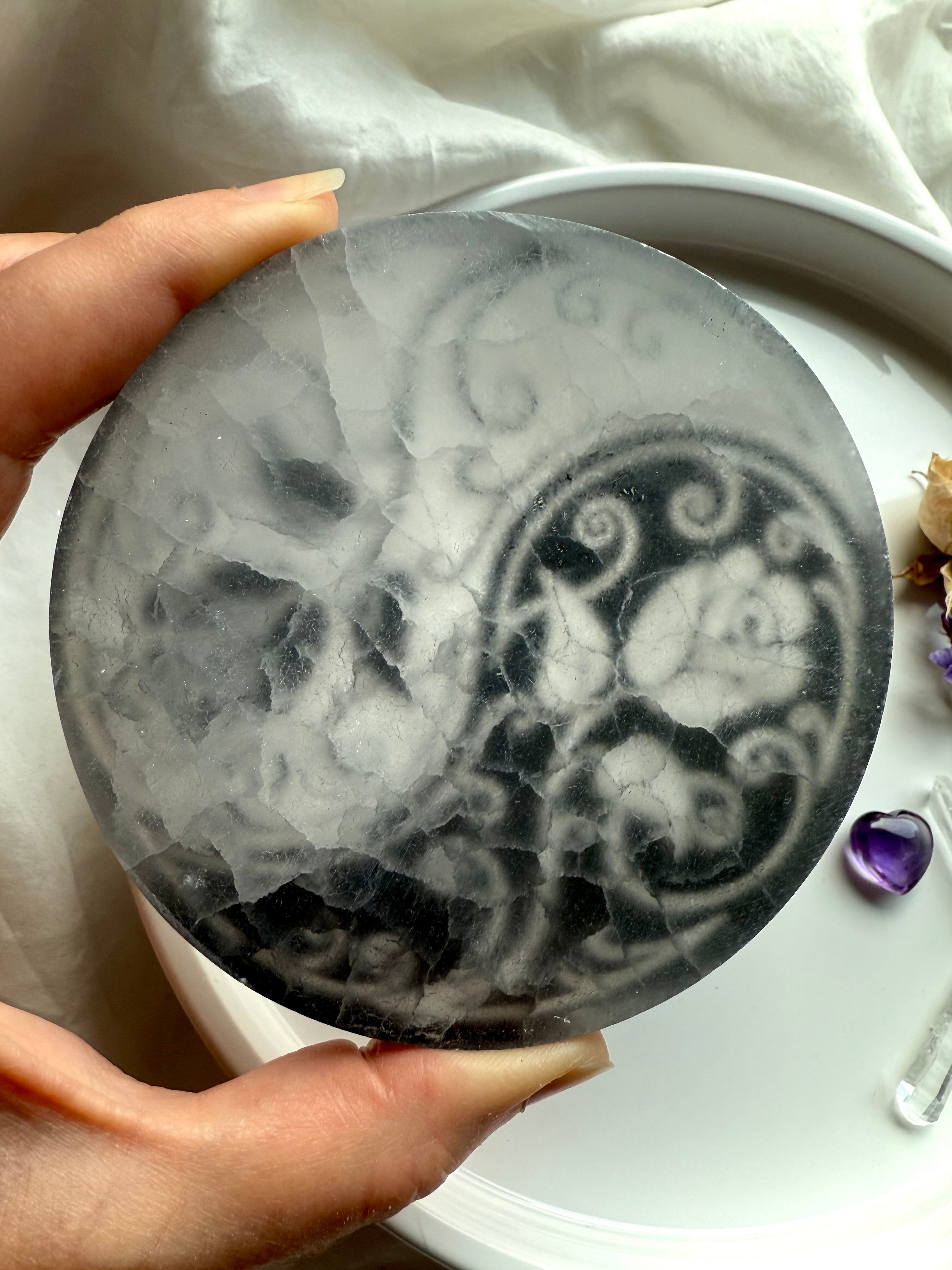 Backside of translucent selenite charging plate showing natural crystal texture and etched yin yang design