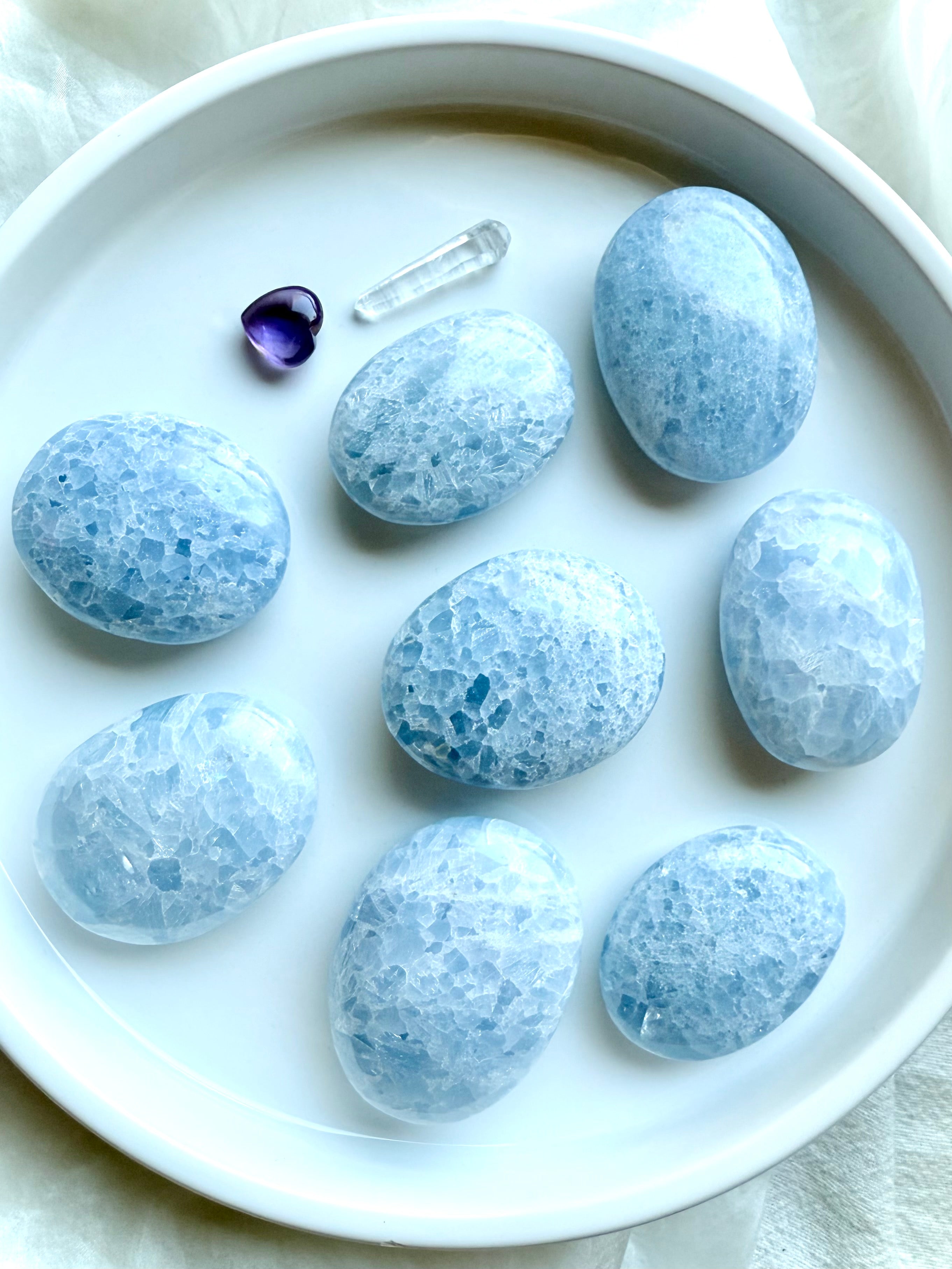 Overhead view of Blue Calcite palm stones arranged in rows on a white background — polished ovals for meditation and relaxation