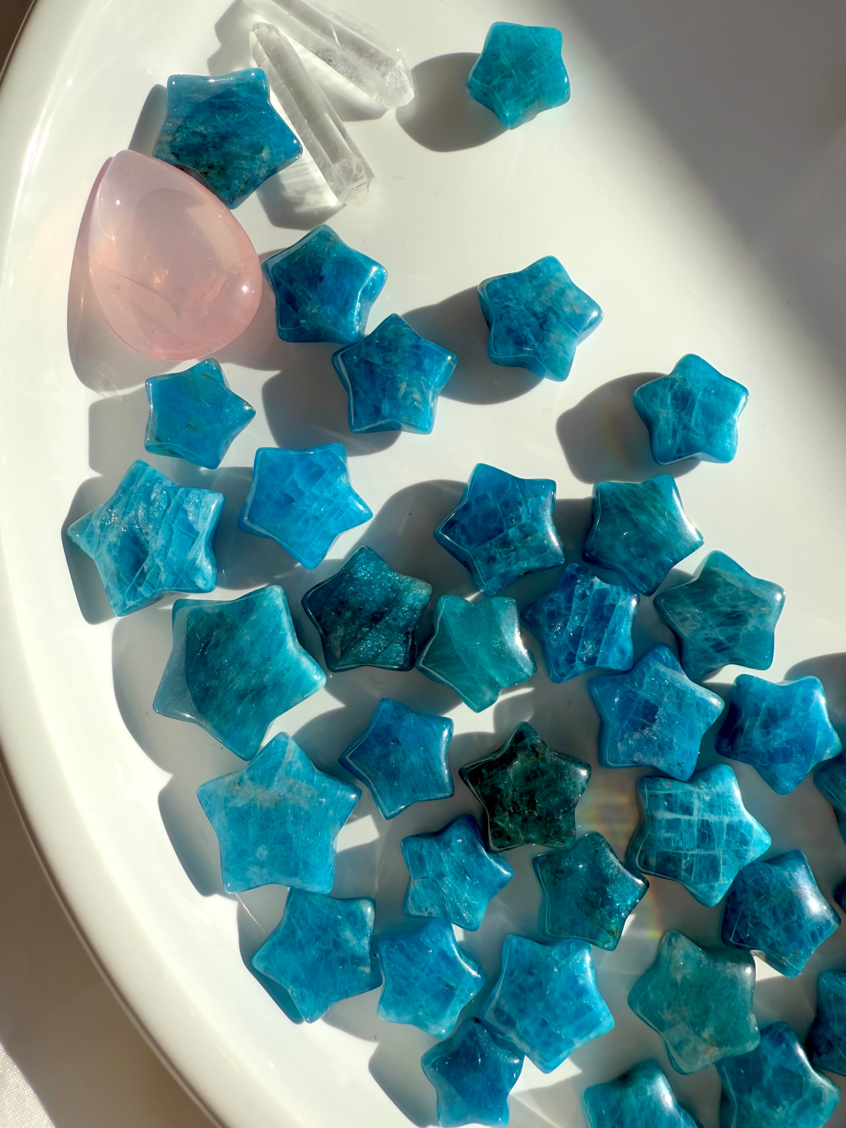 Overhead of Blue Apatite stars on white plate with rose quartz teardrop & quartz points — sweet Throat Chakra arrangement for heart-aligned communication.