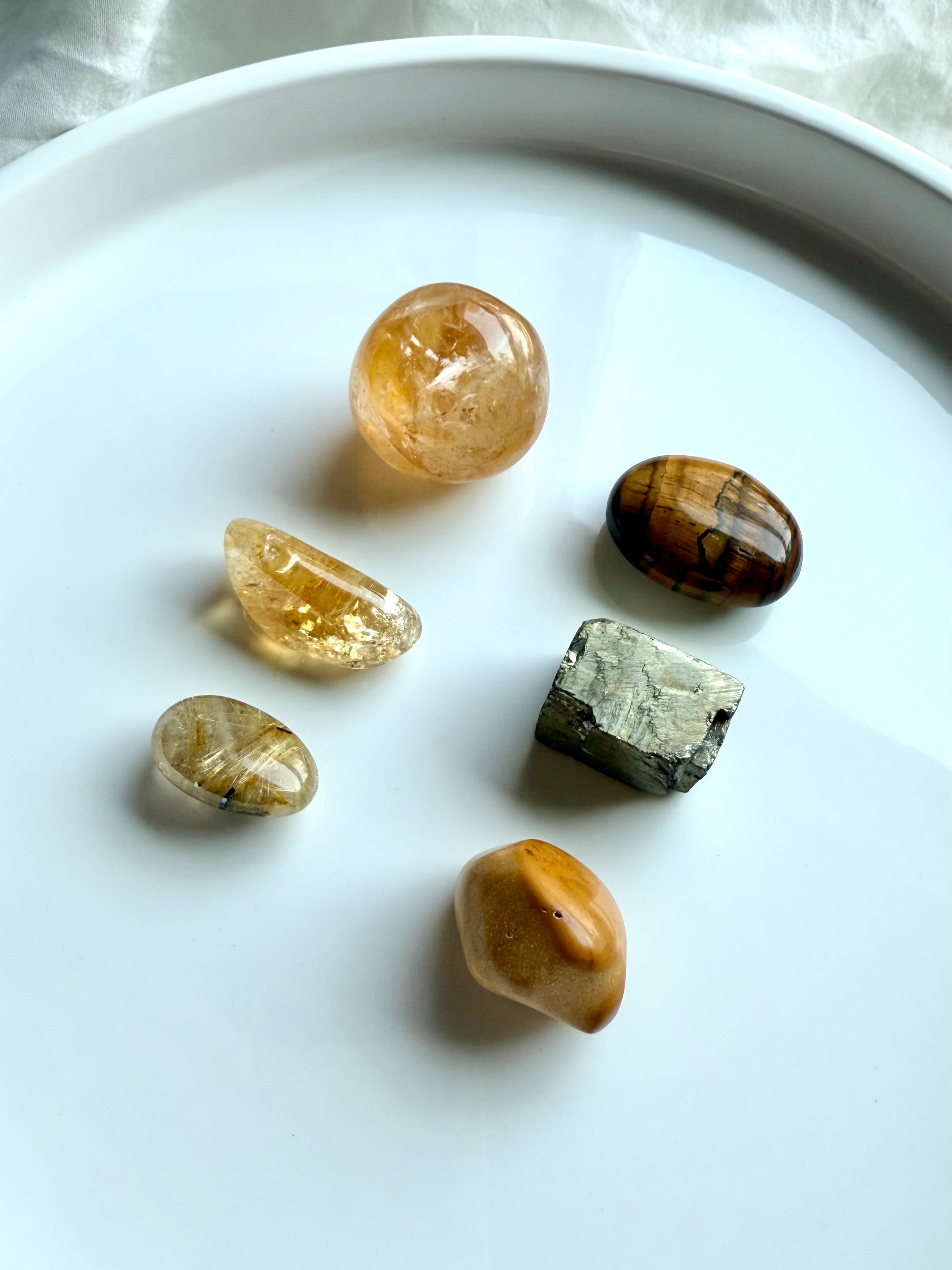 Golden healer, citrine, golden rutile, tiger’s eye, yellow mookaite, and raw pyrite crystals arranged in a grid on white background