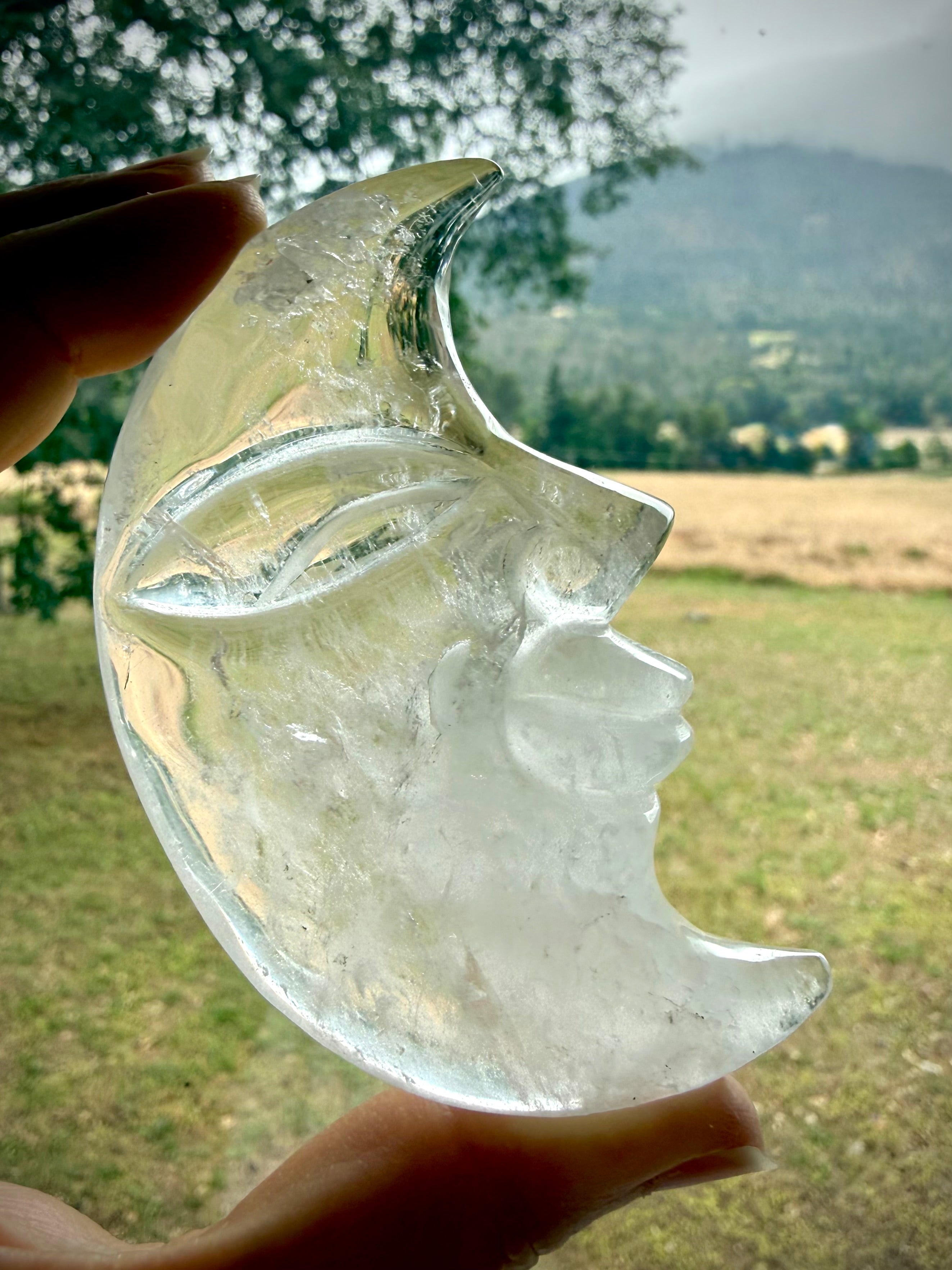 Clear Quartz Moon Face carving glowing in natural light with lovely clarity and detailed celestial crystal craftsmanship