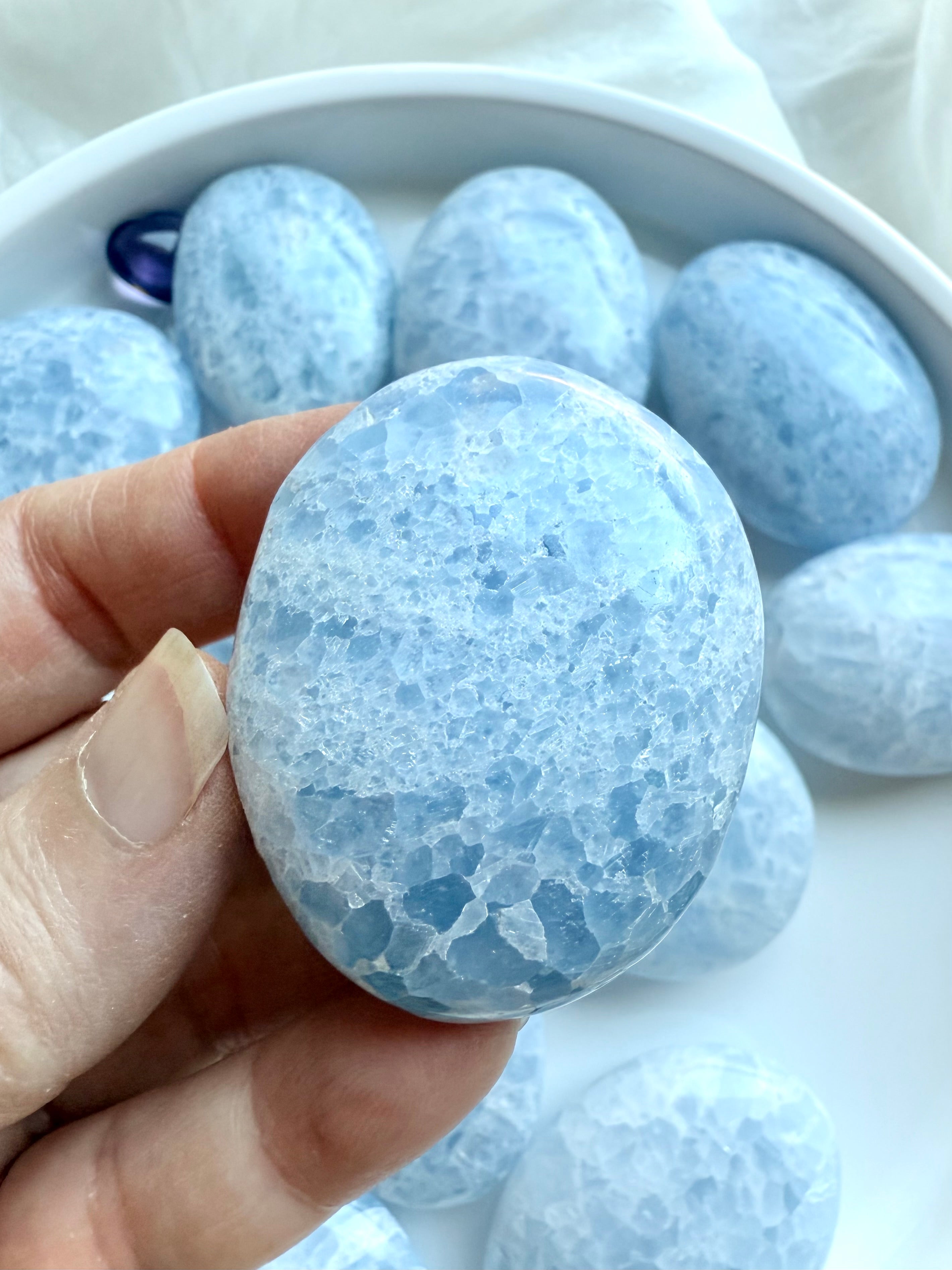 Closeup of a single Blue Calcite palm stone highlighting crystalline patterns and frosty pale blue tones