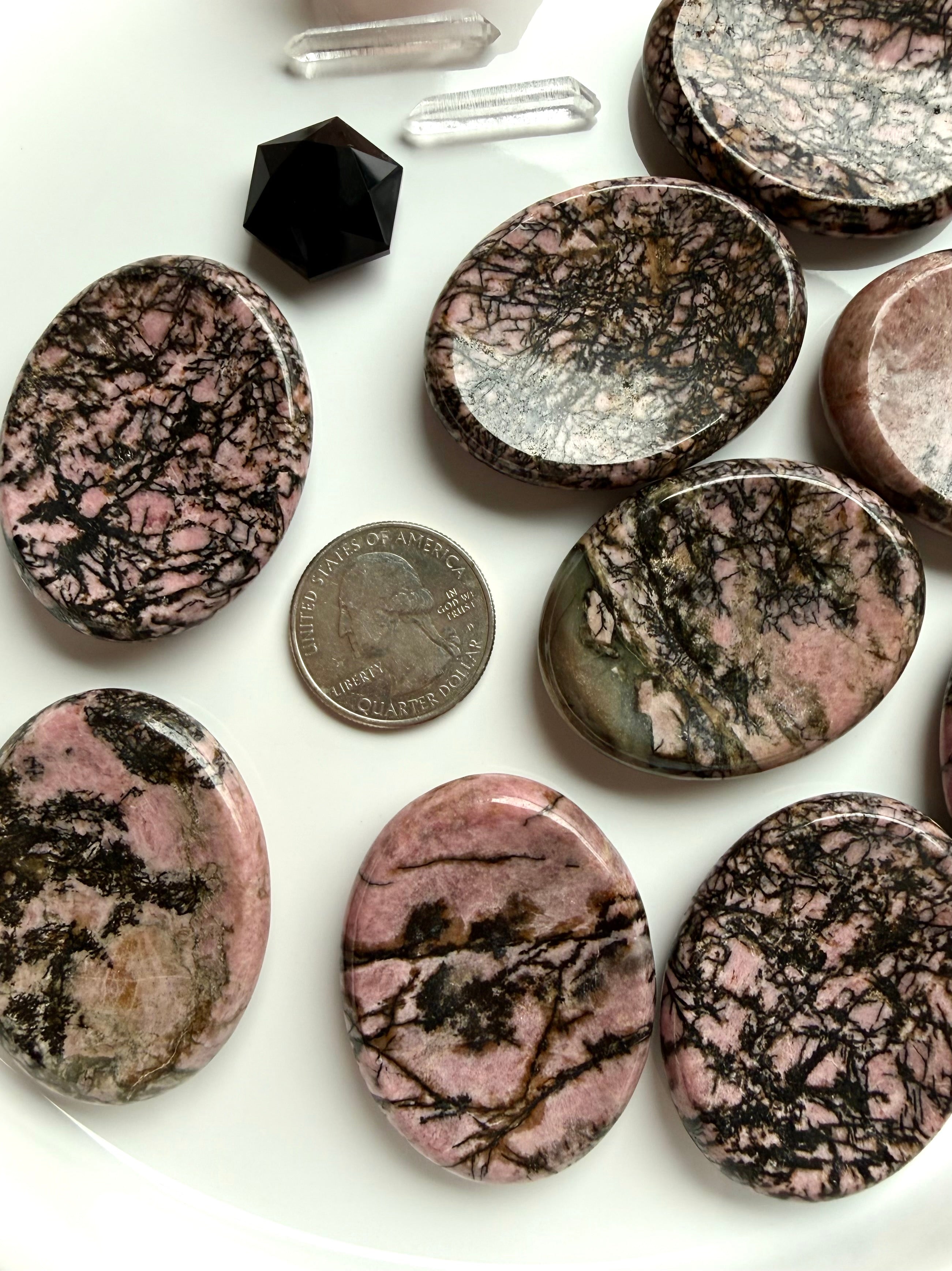 Rhodonite worry stone with US quarter for size comparison on white tray