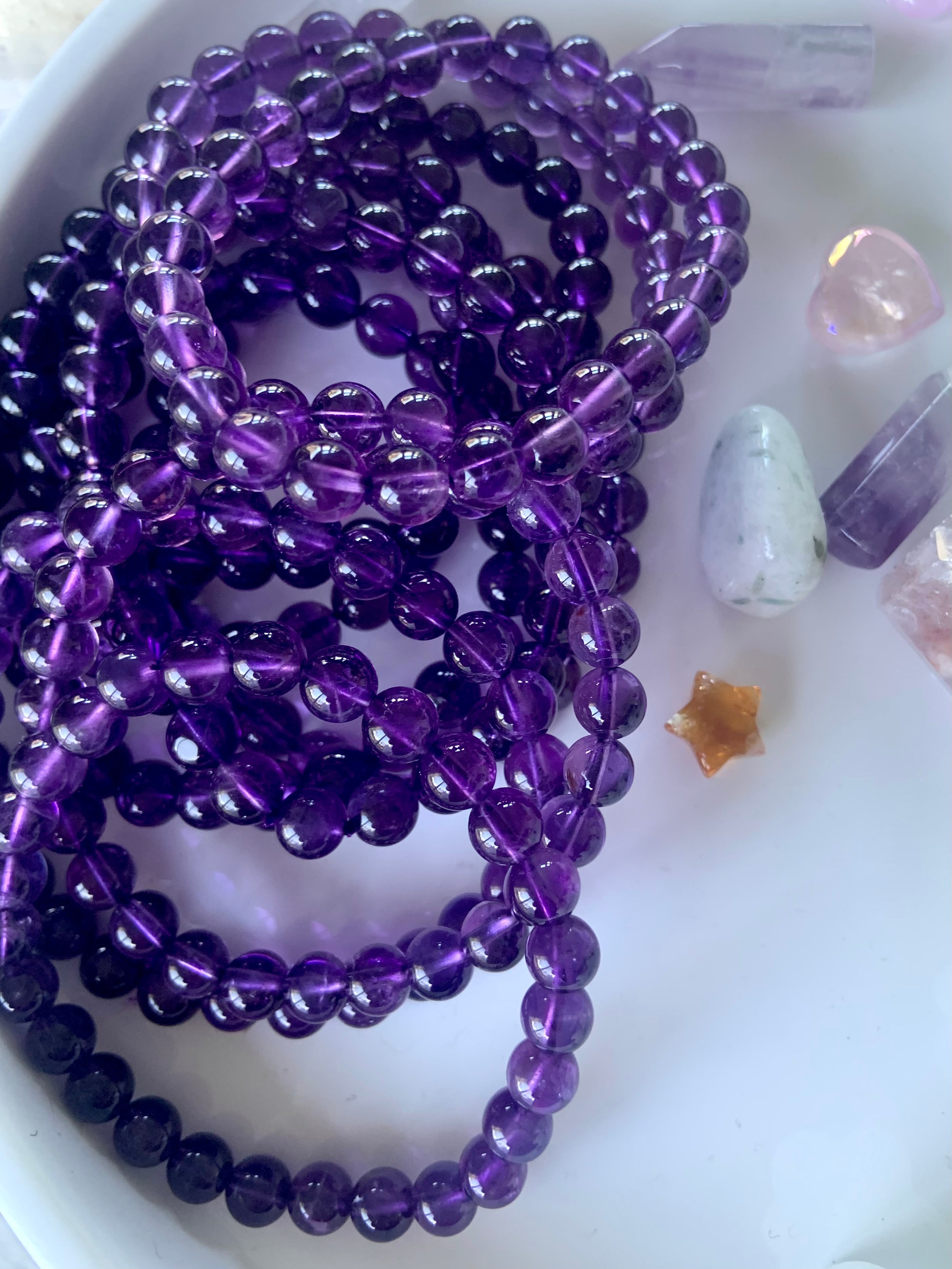 Overhead view of purple amethyst bead bracelets on a white plate with mini crystals in the background