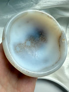 Hand holding White Agate bowl showing inner cloudy patterns and crystal inclusions, healing altar tool for serenity and balance