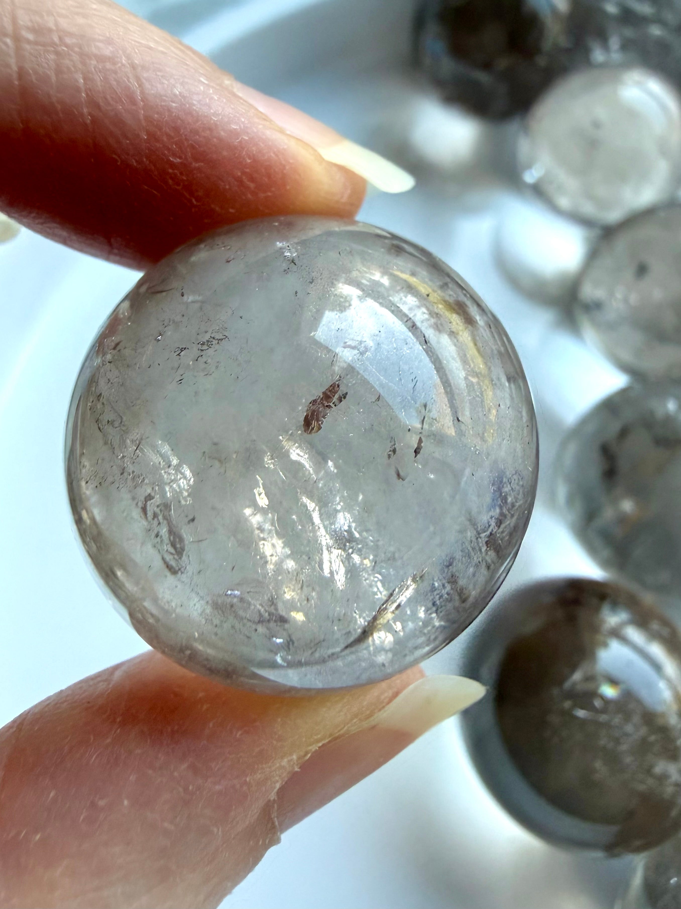 Mini Smoky Quartz crystal sphere close up in hand with internal rainbow flash and natural mineral inclusions