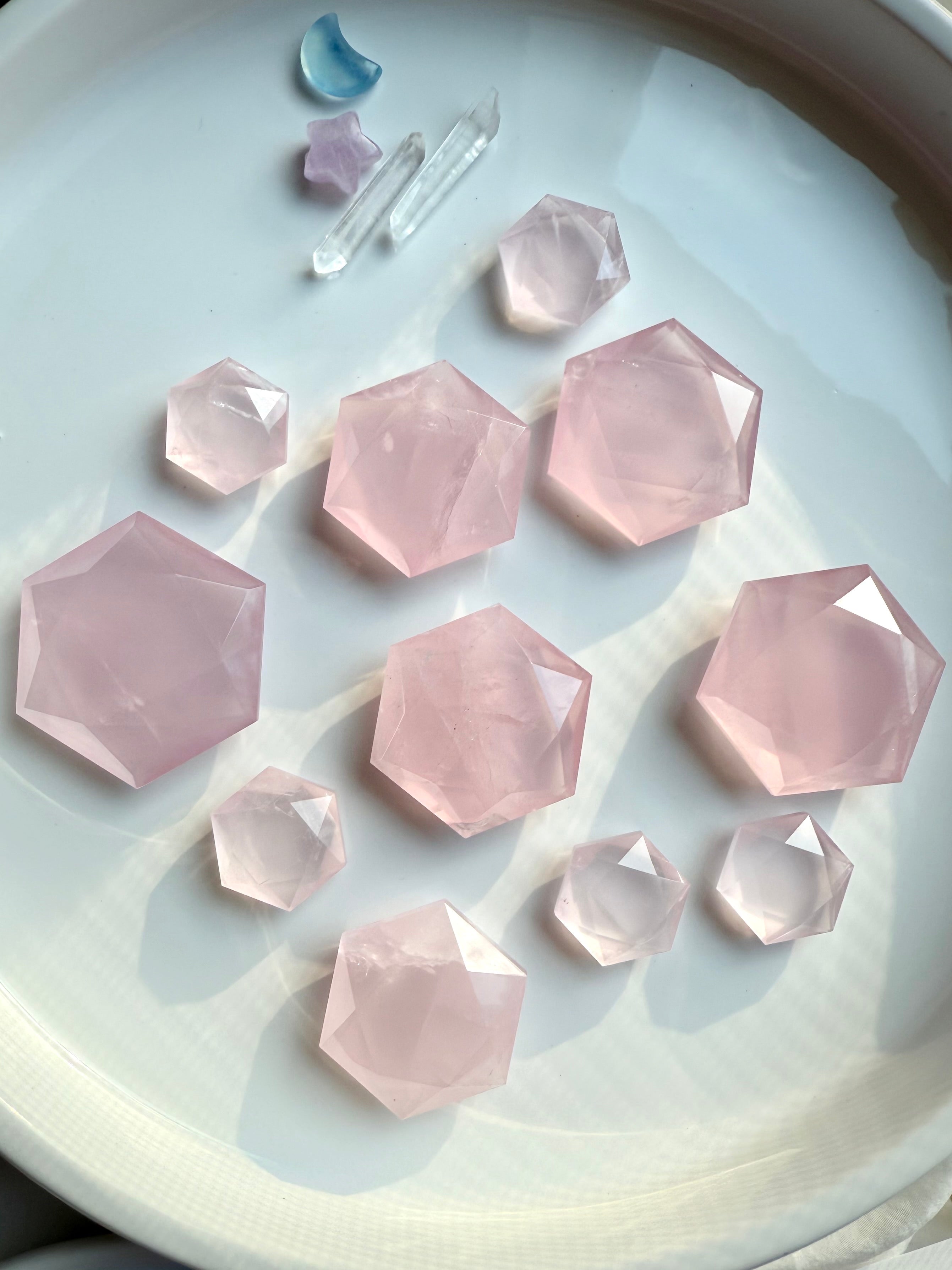 Overhead array of rose quartz hexagon crystals on white background, translucent pink sacred geometry carvings for Heart Chakra healing