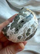Gray Ocean Jasper Crescent Moon with dramatic black orbicular patterns and natural druzy detail, healing palm stone for grounding and inner strength