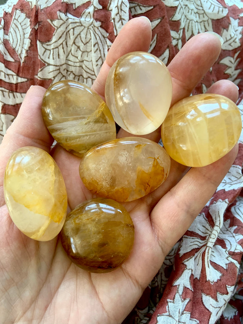 Small Golden Healer Quartz Palm stones shown in indirect natural light on my hand