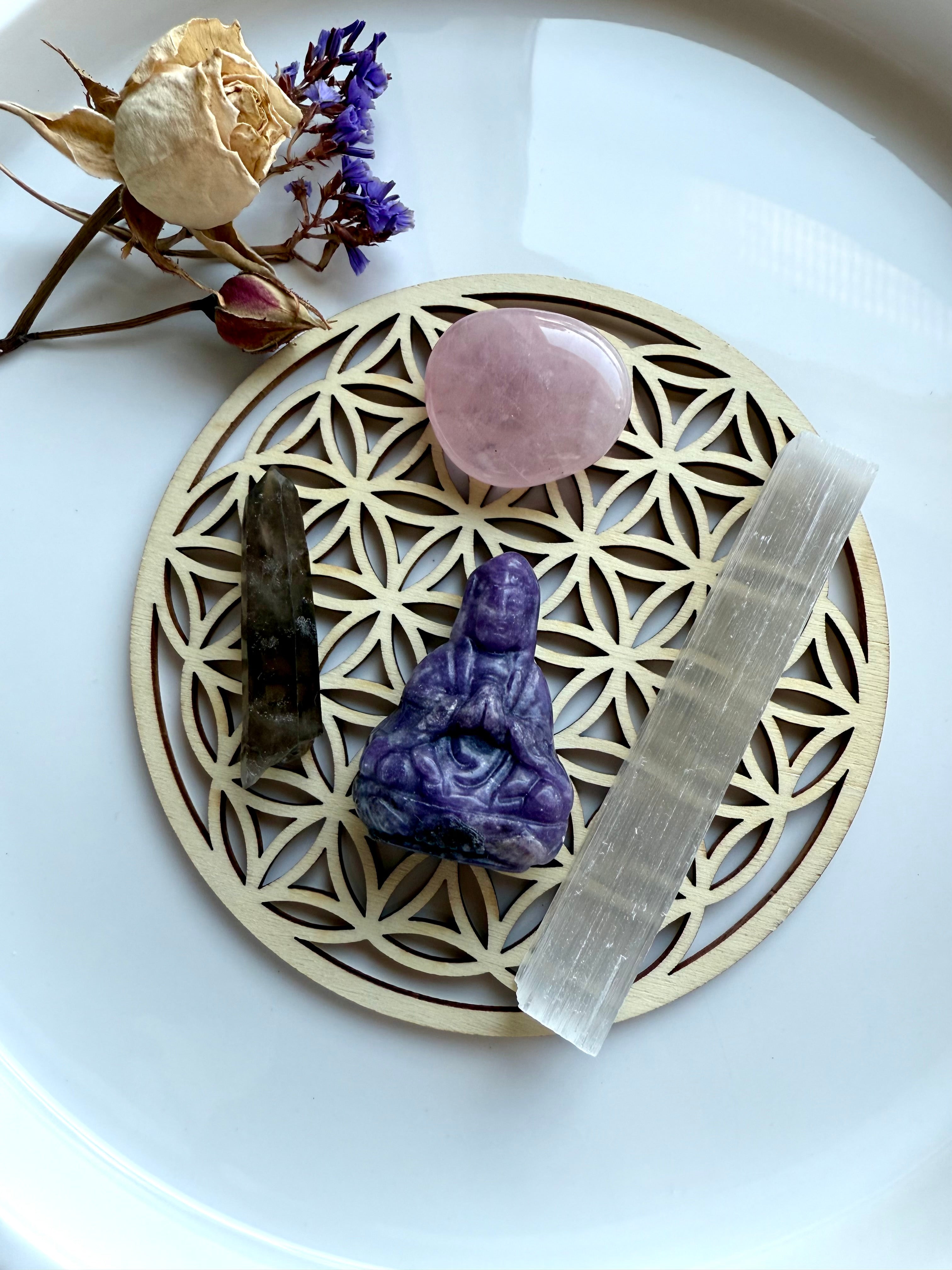 Rose quartz, smoky quartz, selenite wand, and lepidolite Quan Yin figurine on flower of life grid with dried flowers