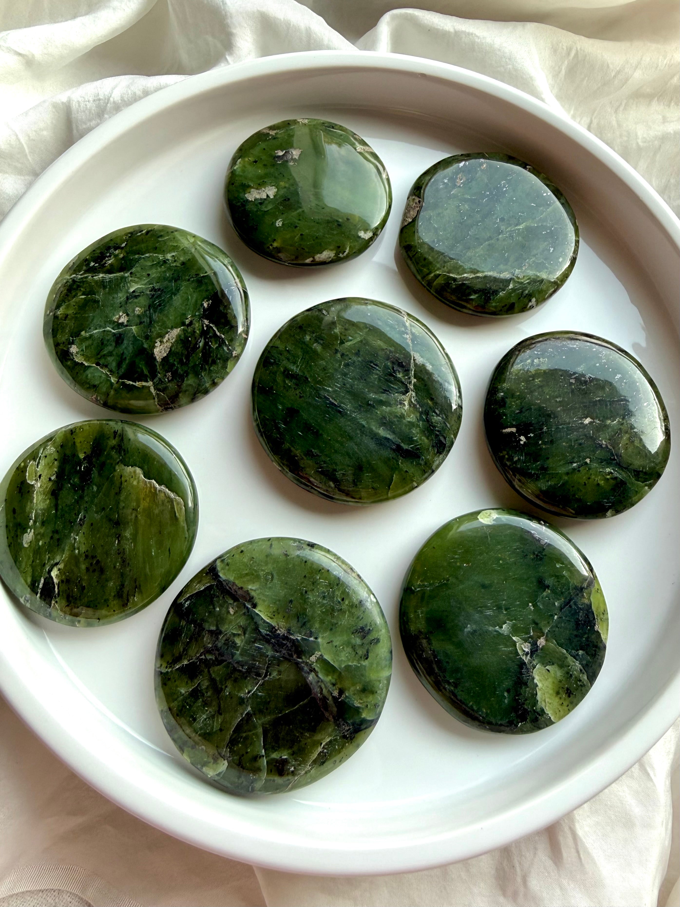 Nephrite jade palm stones on white background highlighting rich forest green tones and natural mineral patterns, grounding crystal for meditation