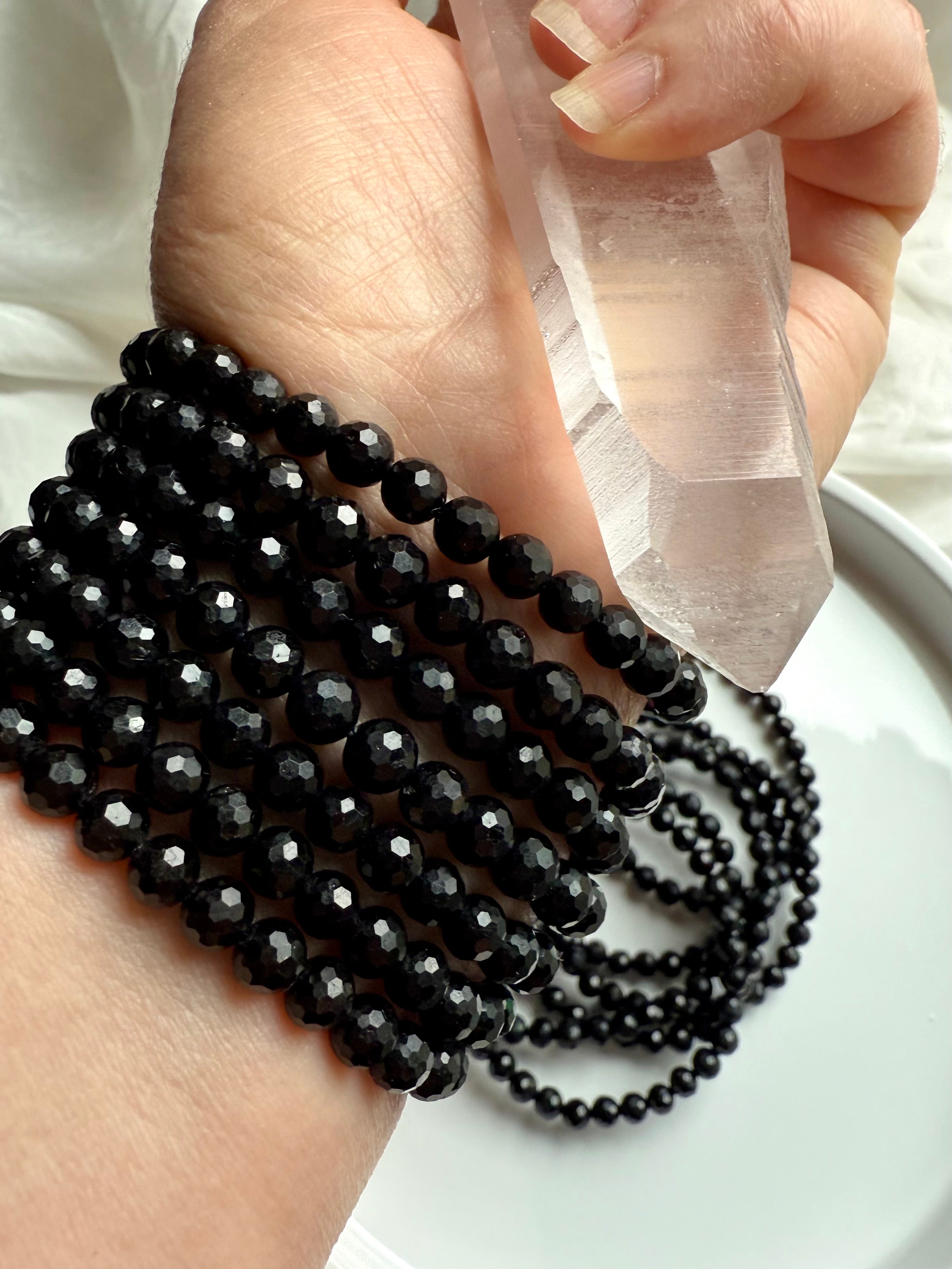 hand holding clear quartz wand with multiple faceted black tourmaline bracelets wrapped around wrist