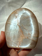 Peach Moonstone freeform held in hand showing bright silvery Moonstone glow across the polished face