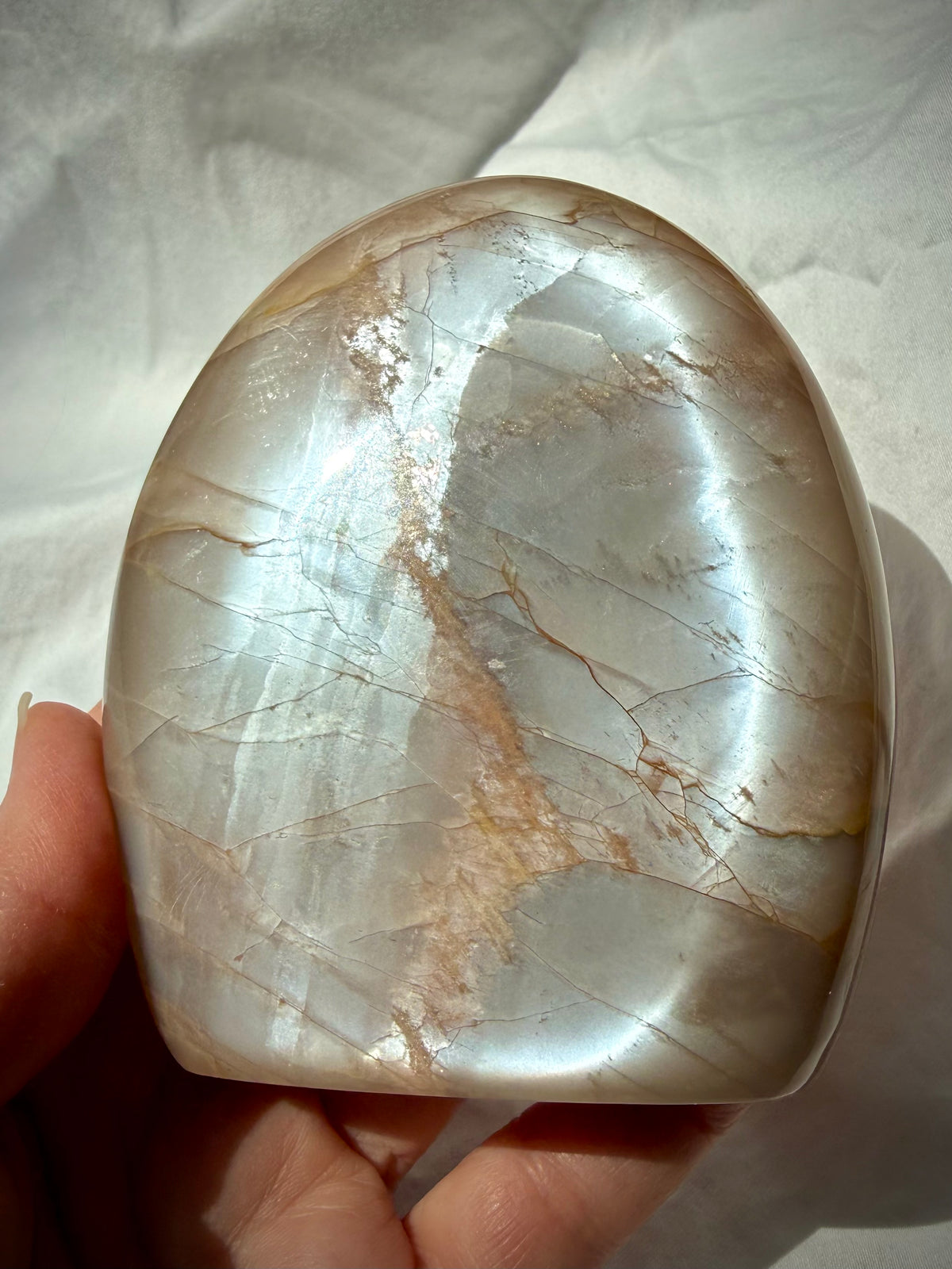 Peach Moonstone freeform held in hand showing bright silvery Moonstone glow across the polished face
