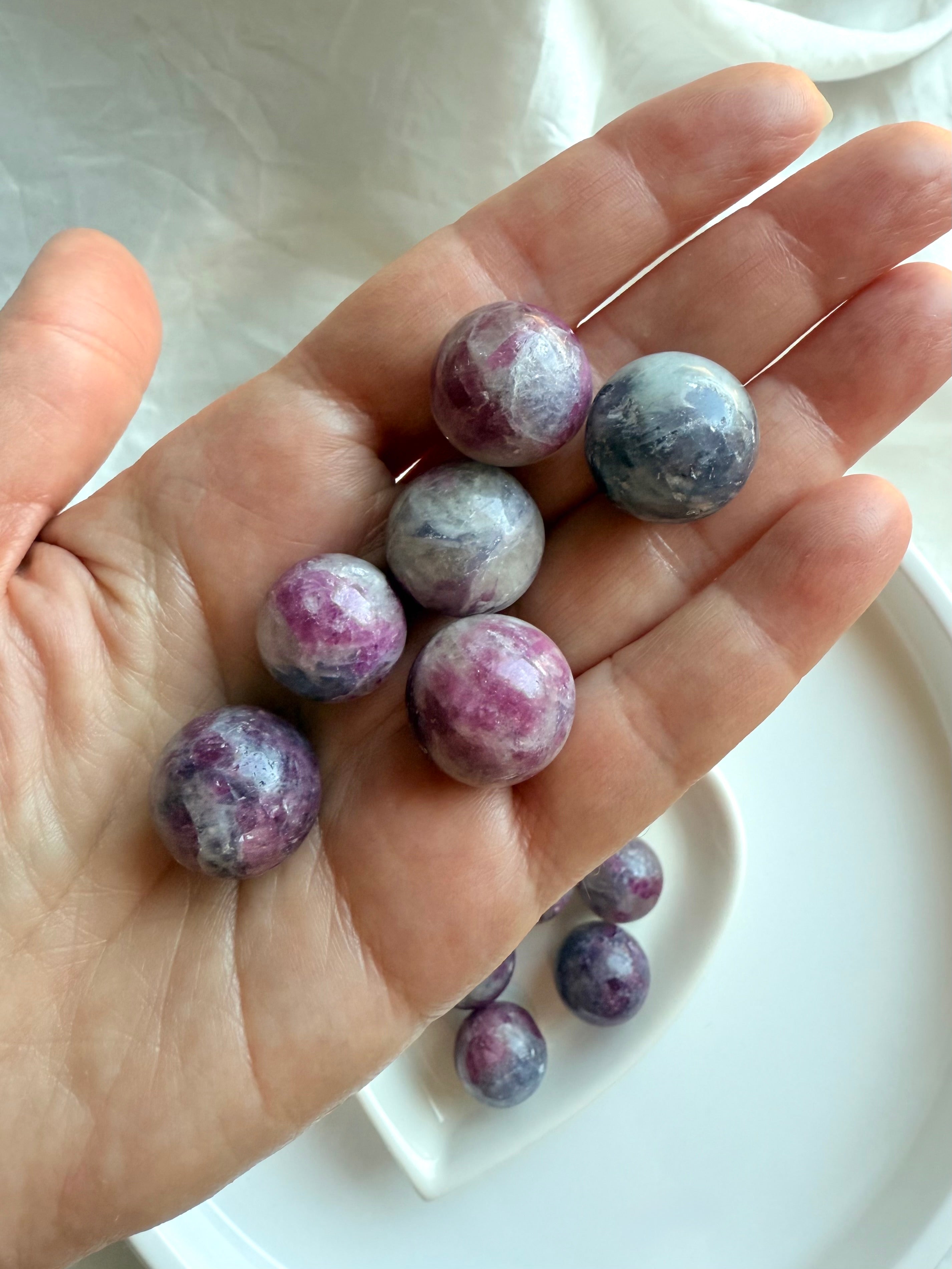 Hand holding several polished Mini Unicorn Stone spheres showing natural pink, purple, and gray tones