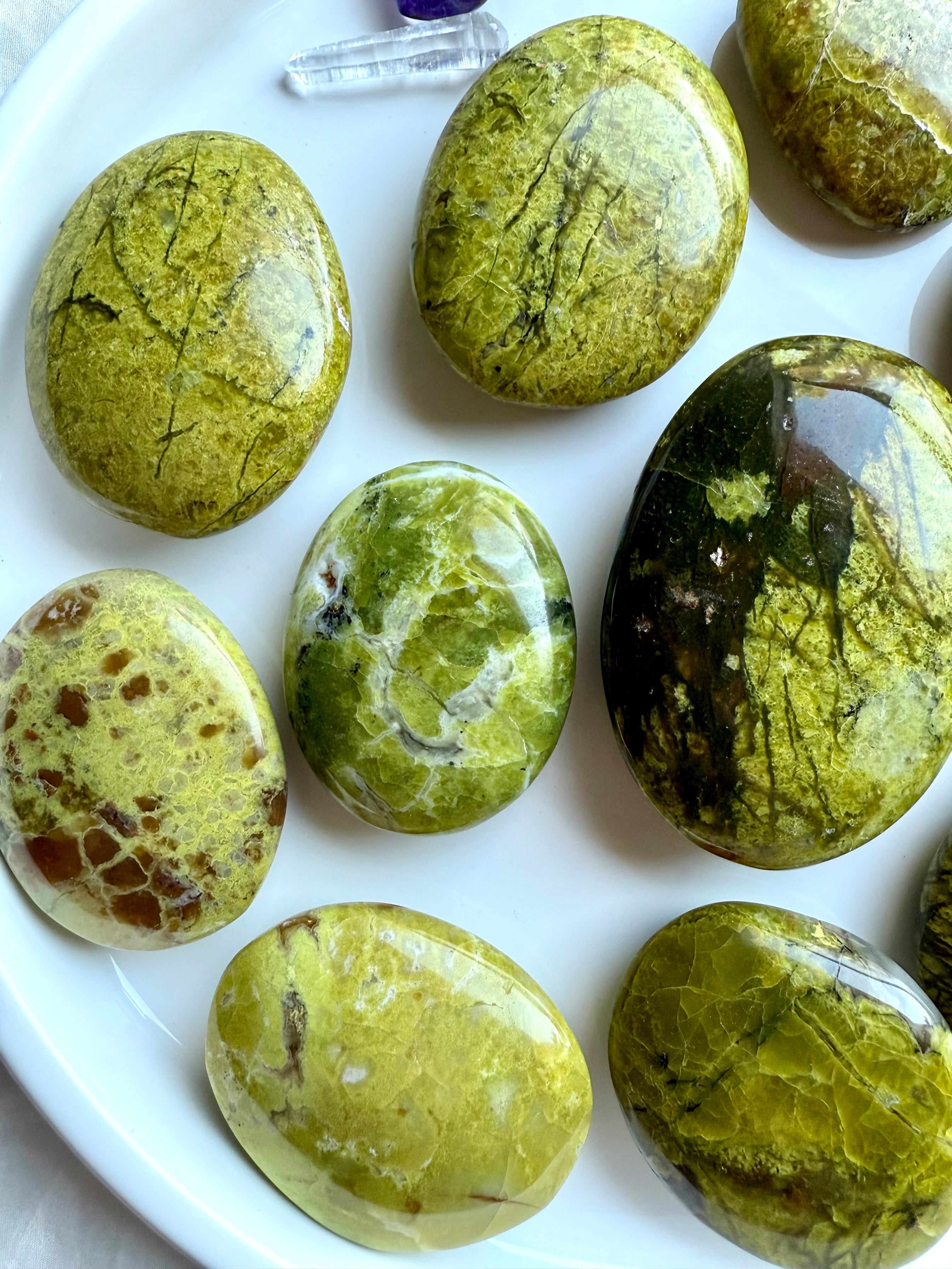 Mid-range view of Green Opal palm stones on a white plate — polished oval crystals in luminous chartreuse tones for heart chakra healing and emotional renewal.