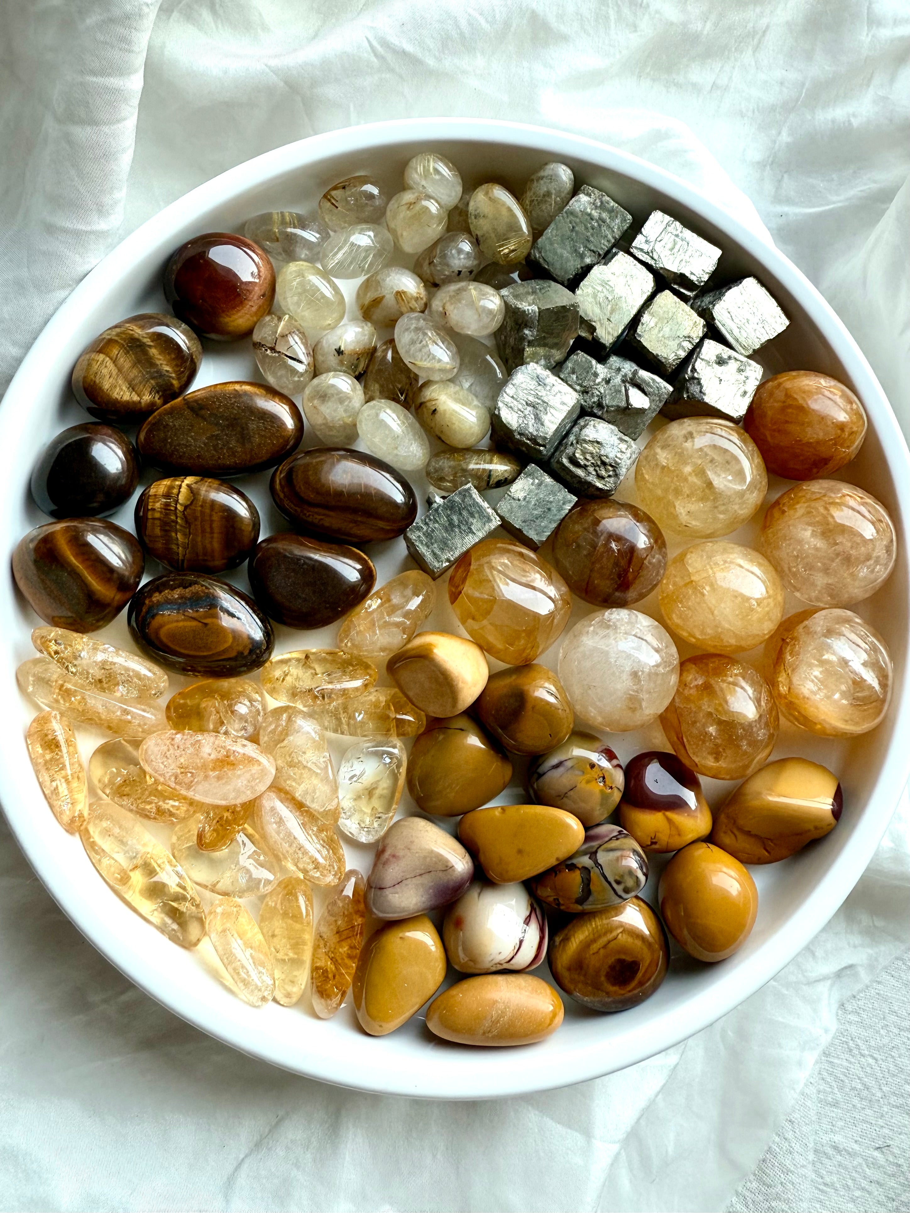 Solar Plexus Chakra crystals arranged in segmented pie slices on a white plate — golden healer, citrine, golden rutile, tiger’s eye, yellow mookaite, and raw pyrite