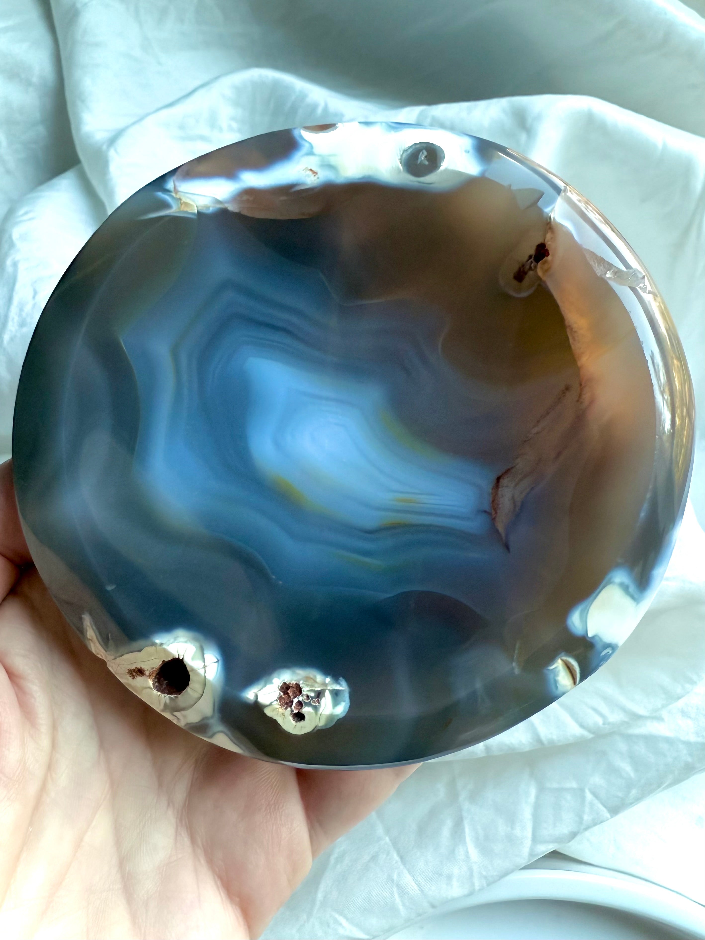 Hand holding glossy Orca Agate bowl showing soothing blue-grey banding and natural druzy pockets for forgiveness work