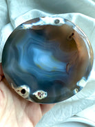 Hand holding glossy Orca Agate bowl showing soothing blue-grey banding and natural druzy pockets for forgiveness work