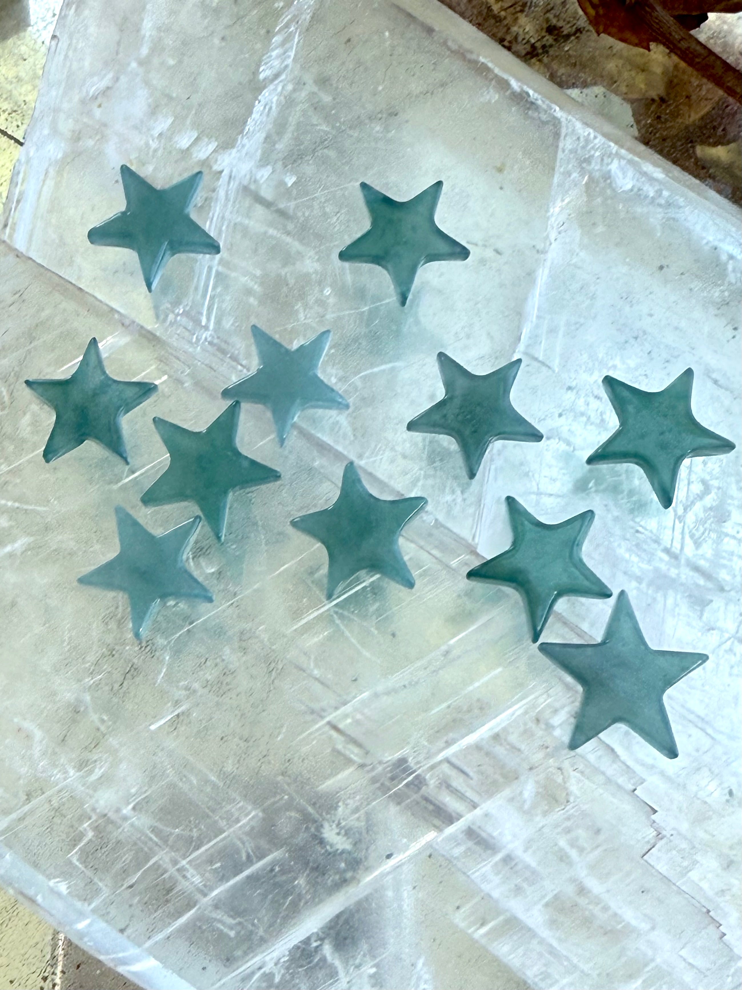 Mini Blue Water Jade Stars photographed on a selenite slab in natural indirect lighting