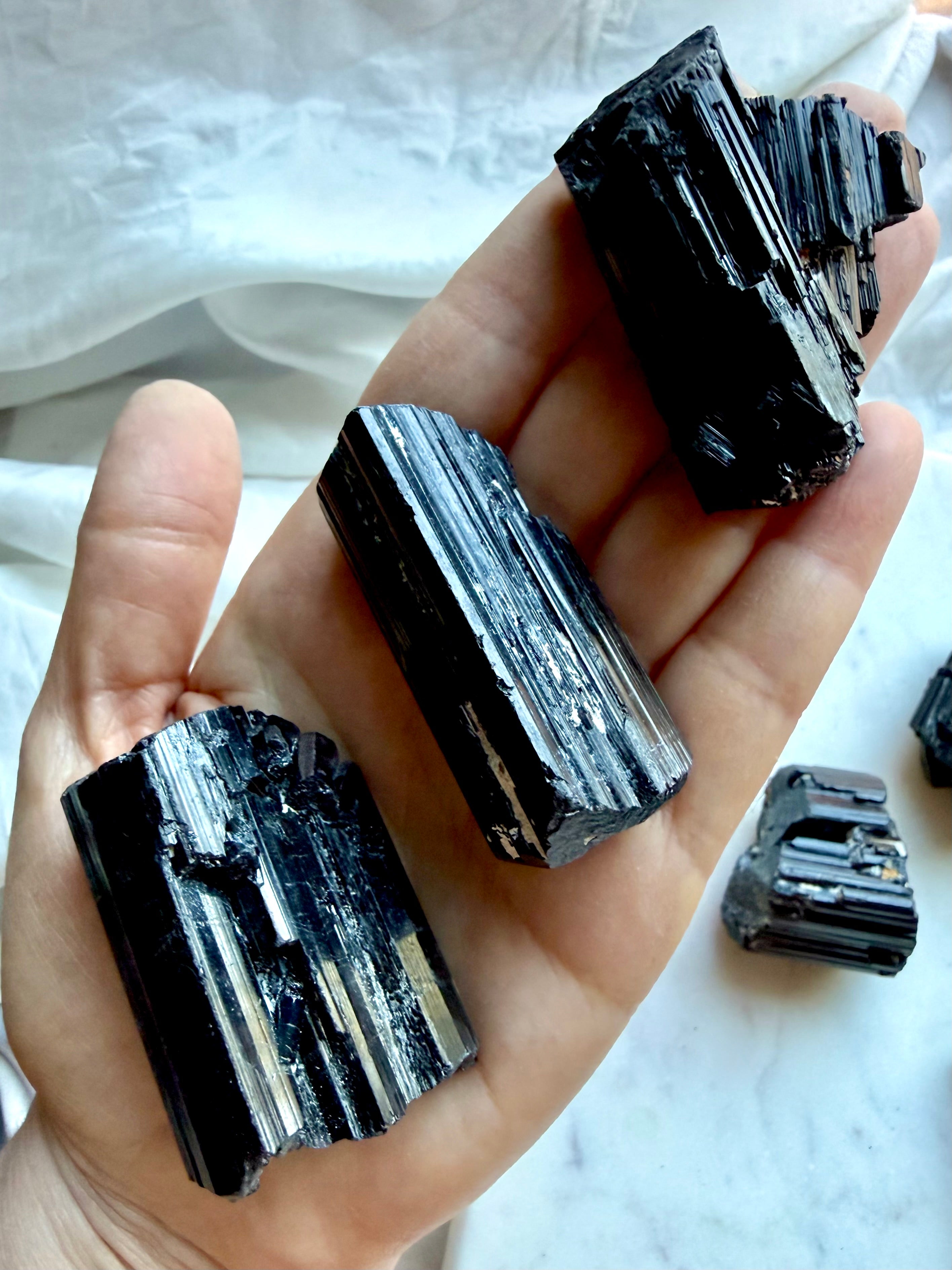 Raw Black Tourmaline crystals held in hand showing varied sizes, rough surfaces, and glossy striations