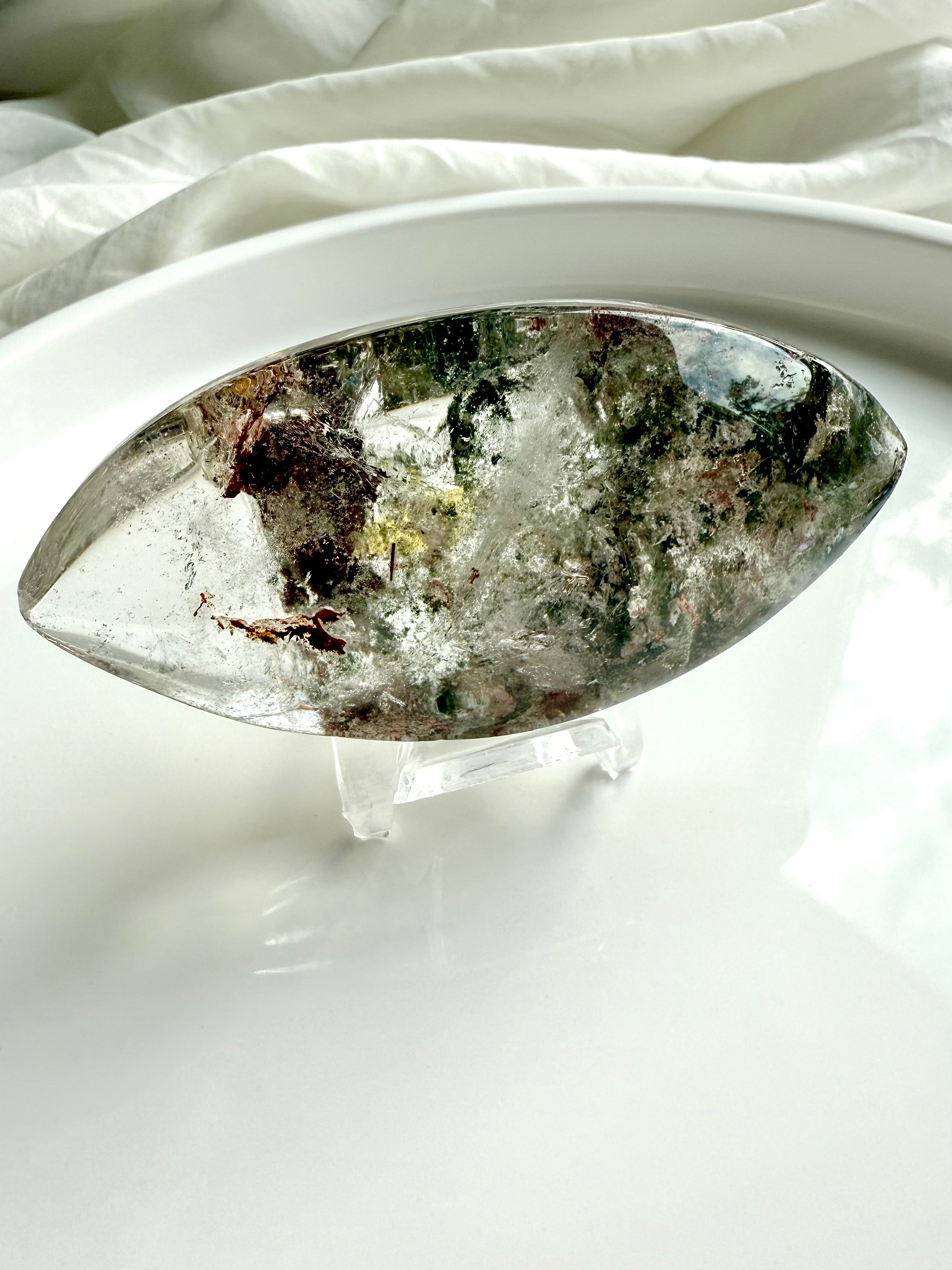 Garden Quartz marquise lens with scenic lodolite and golden healer inclusions displayed on clear stand