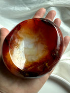 Hand holding Carnelian crystal bowl, displaying polished interior with fiery red and white banded patterns.