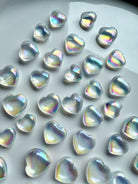 Tray filled with iridescent mini opal aura quartz crystal hearts glowing with rainbow light