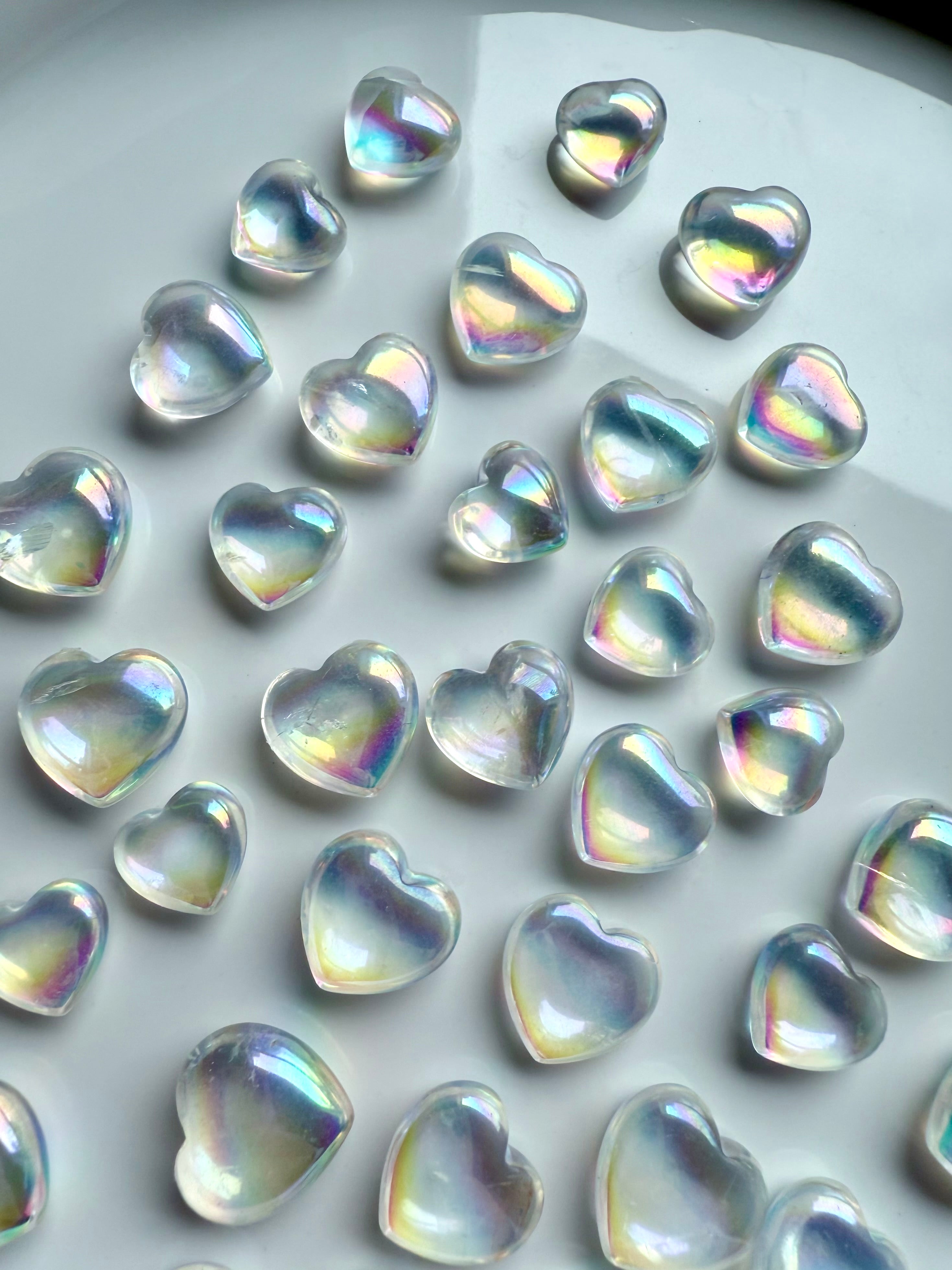 Tray filled with iridescent mini opal aura quartz crystal hearts glowing with rainbow light