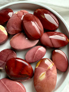 polished Mookaite Jasper palm stones in earthy red and mauve tones for grounding, strength, vitality, and emotional balance