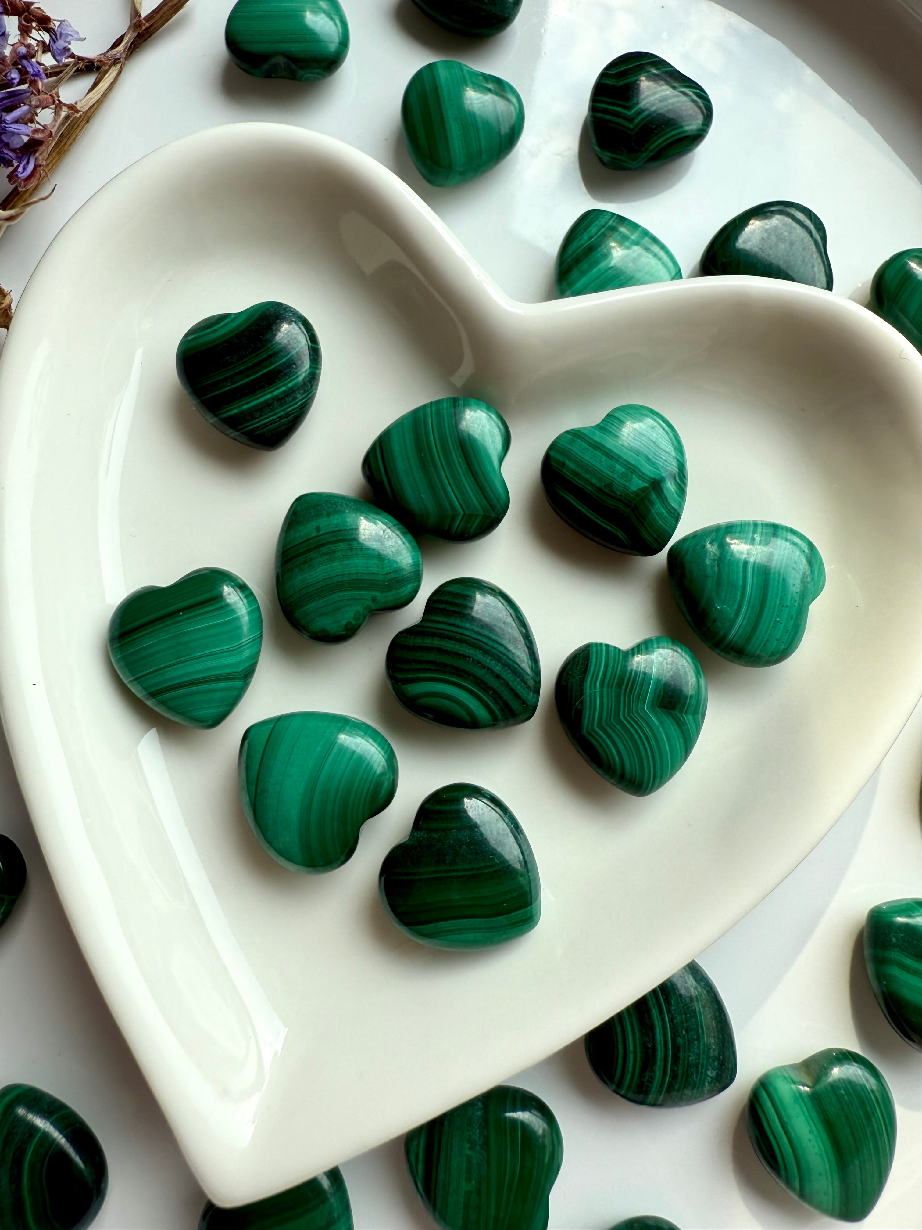Detail view of polished Mini Malachite hearts in white heart bowl showcasing layered greens, bubbles, and chatoyant texture