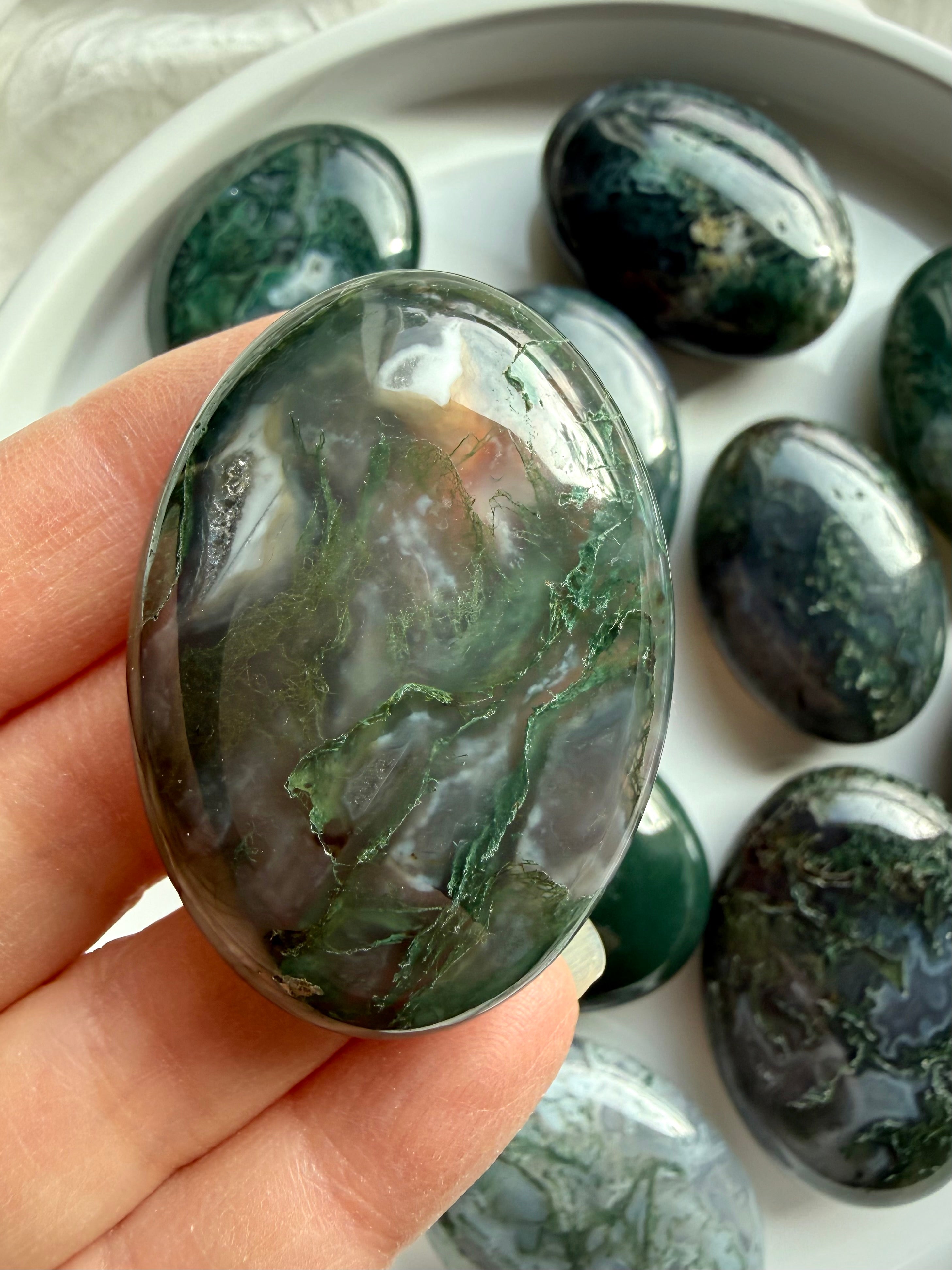Polished moss agate palm stone resting in palm, earthy green crystal for emotional balance and grounding energy