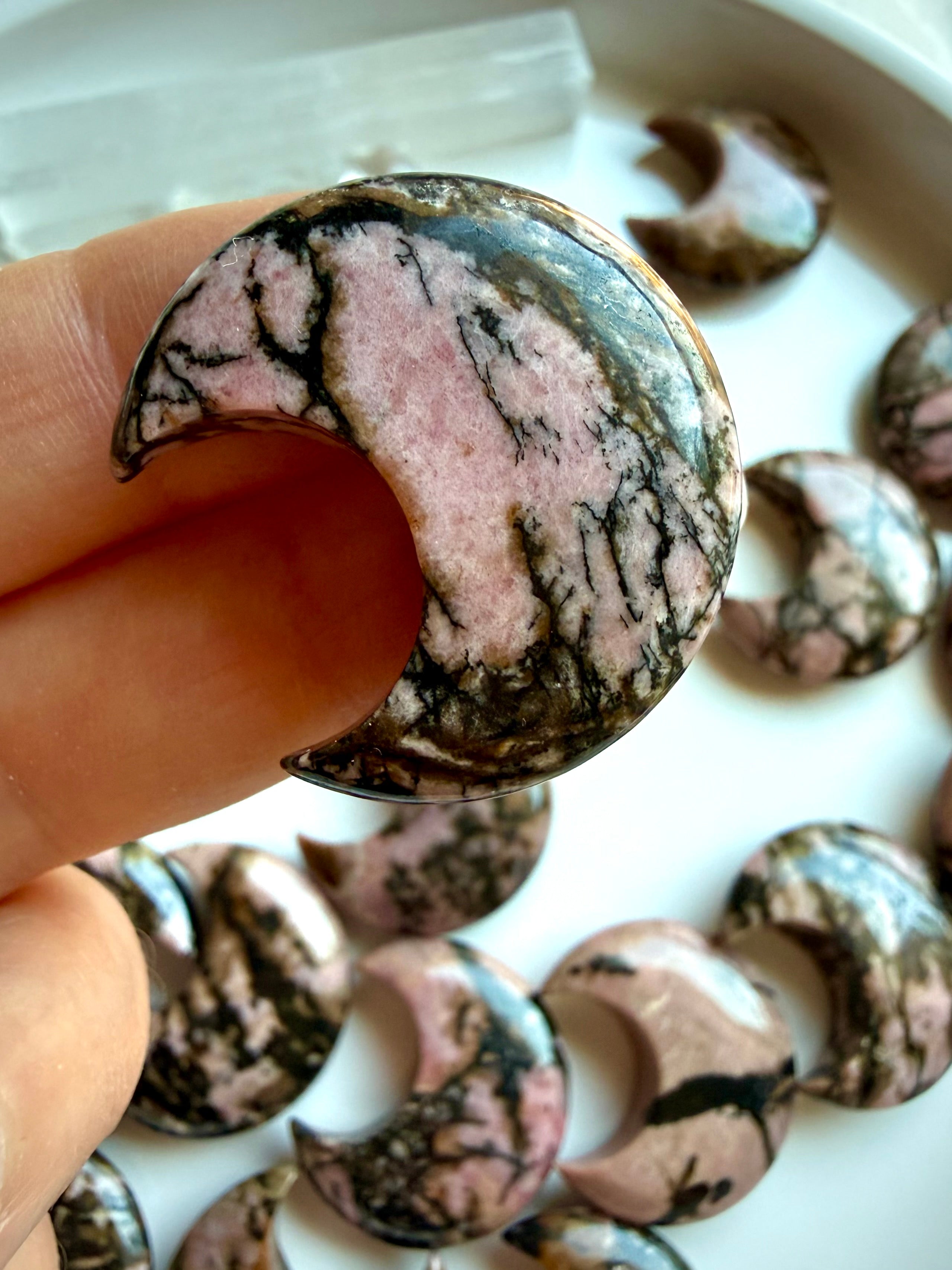Close-up of polished Rhodonite moon carvings displaying natural pink stone with black manganese veining