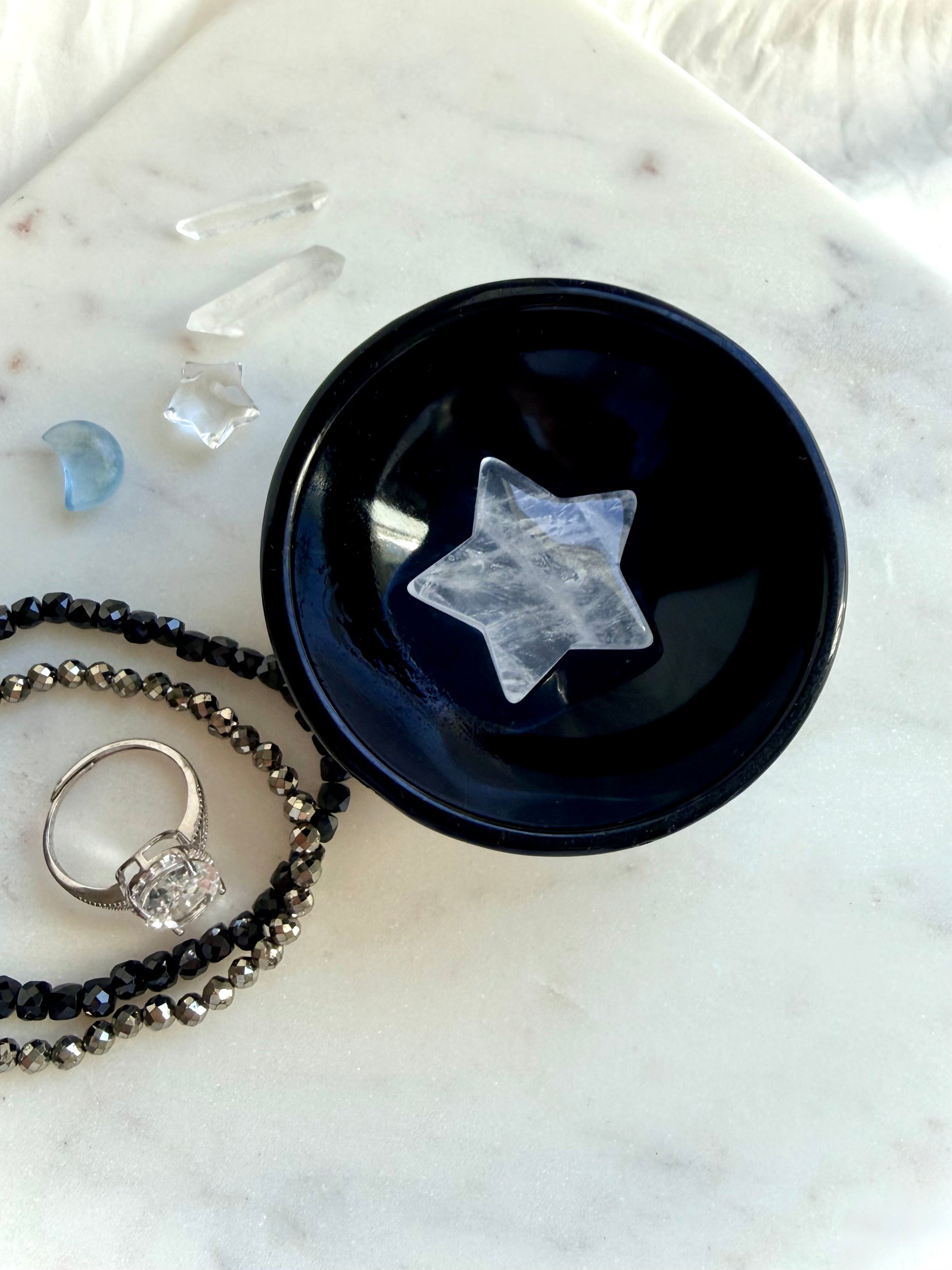 Black Obsidian bowl holding Clear Quartz star carving beside crystal jewelry