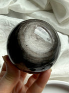 Silver Sheen Obsidian sphere held in hand, a grounding Root Chakra crystal for protection, clarity, and intuitive insight