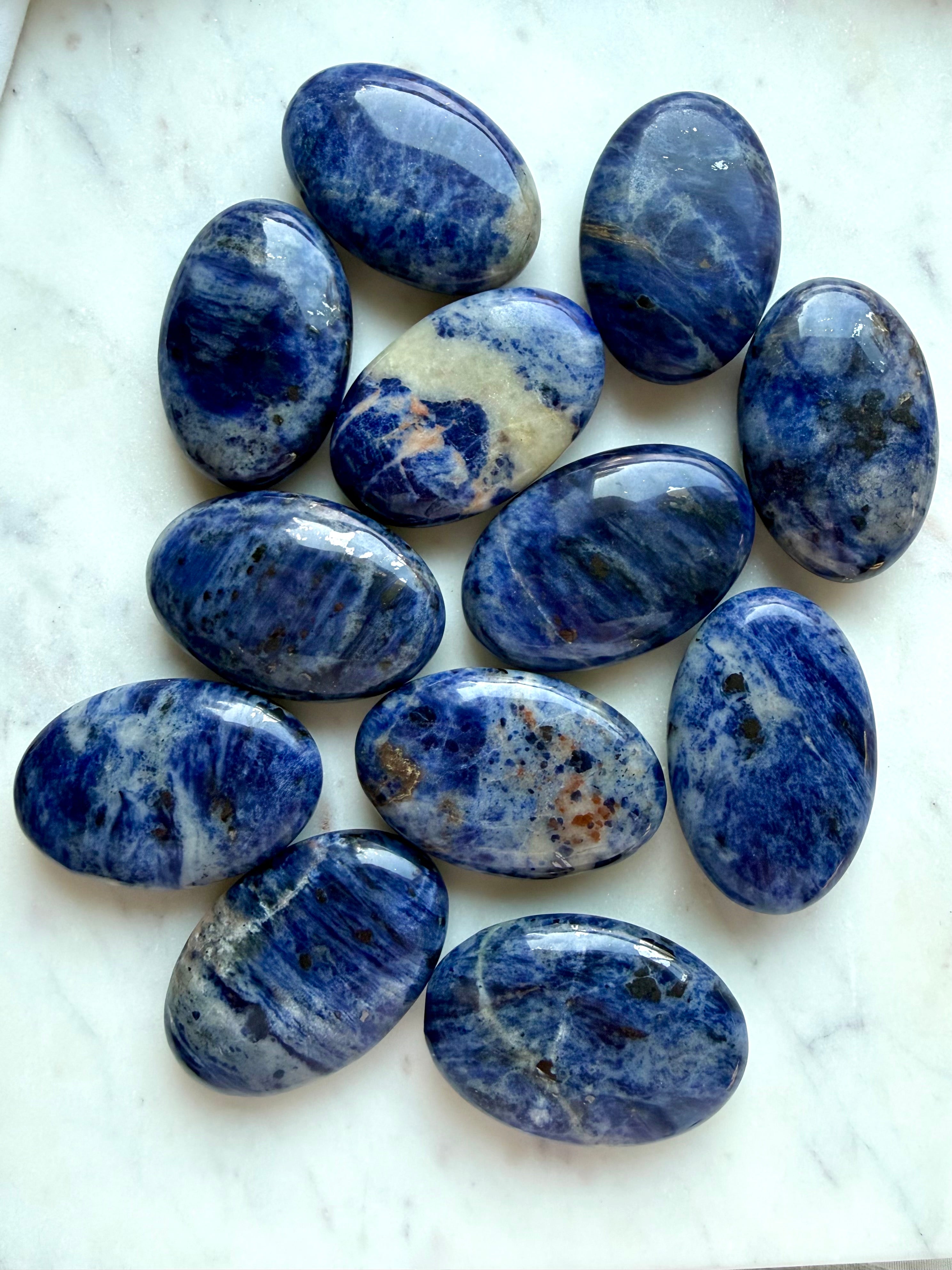 Polished Sodalite palm stones with deep blue color, cloudy white veining, and natural pattern variation