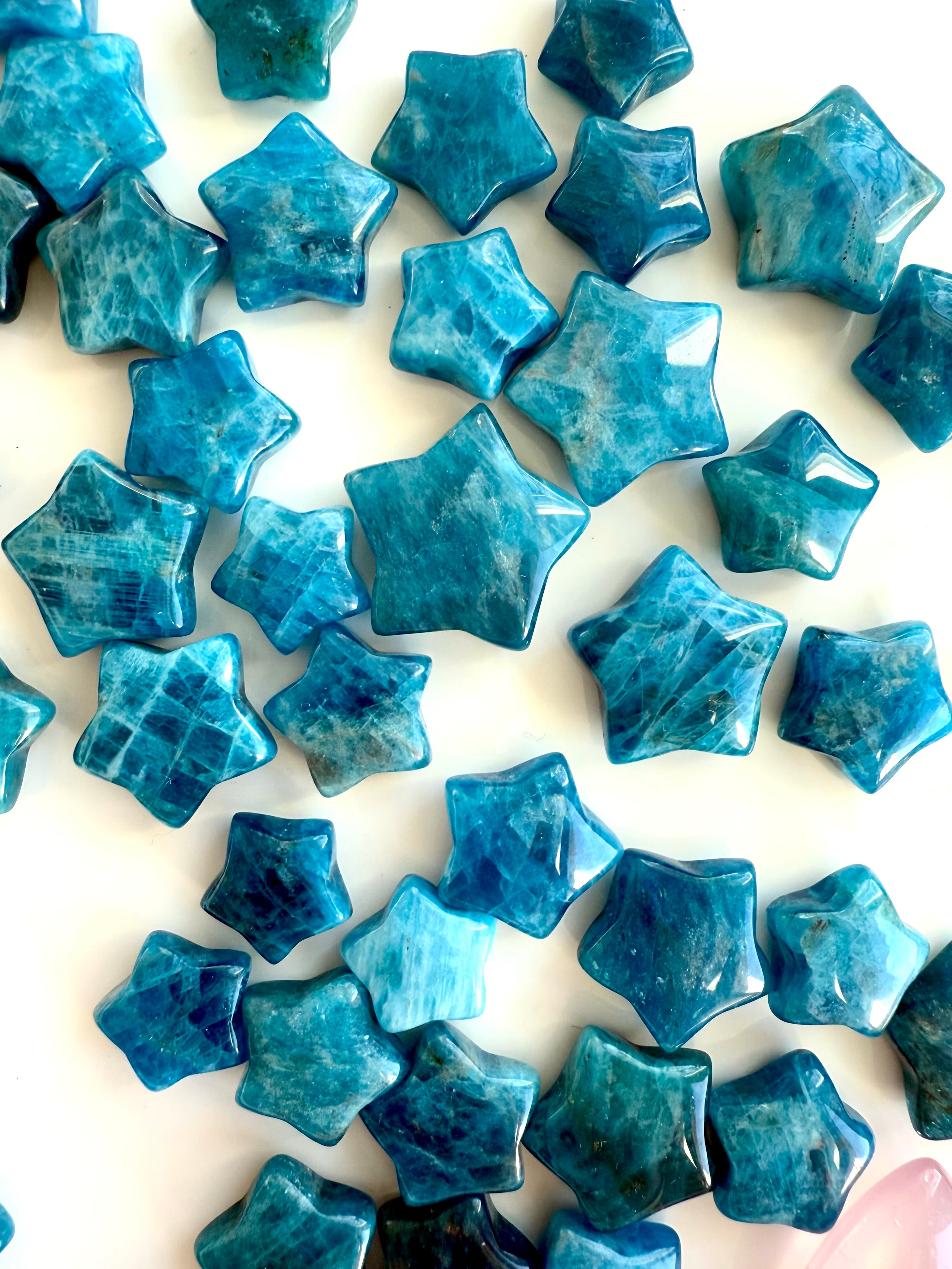 Close-up of Blue Apatite mini crystal stars on white background — showing teal color patterns, flash, and natural variations in each star carving.