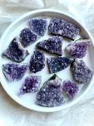 Purple Amethyst geode clusters in assorted sizes displayed on a white plate